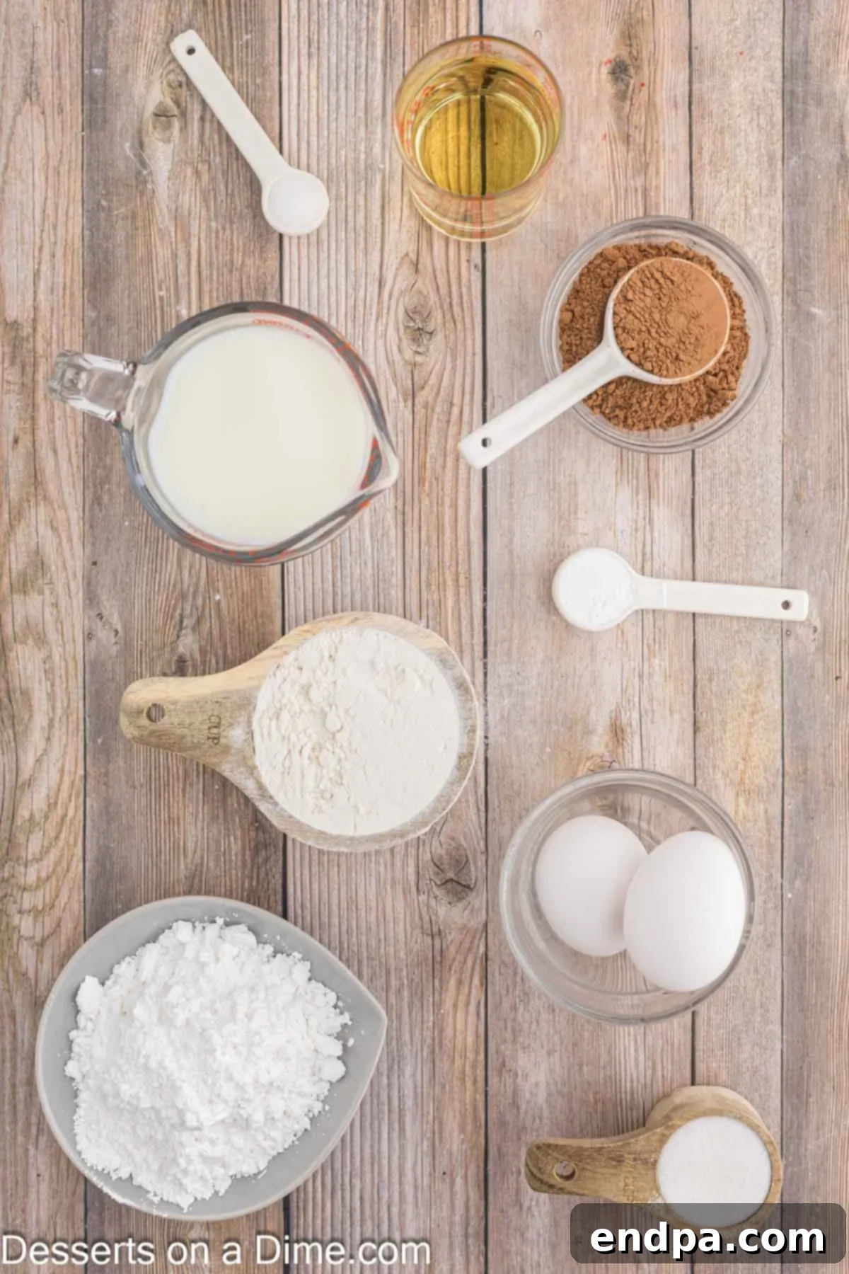 A flat lay of the key ingredients for chocolate funnel cake: all-purpose flour, unsweetened cocoa powder, milk, sugar, baking powder, salt, eggs, vegetable oil, and powdered sugar for dusting.