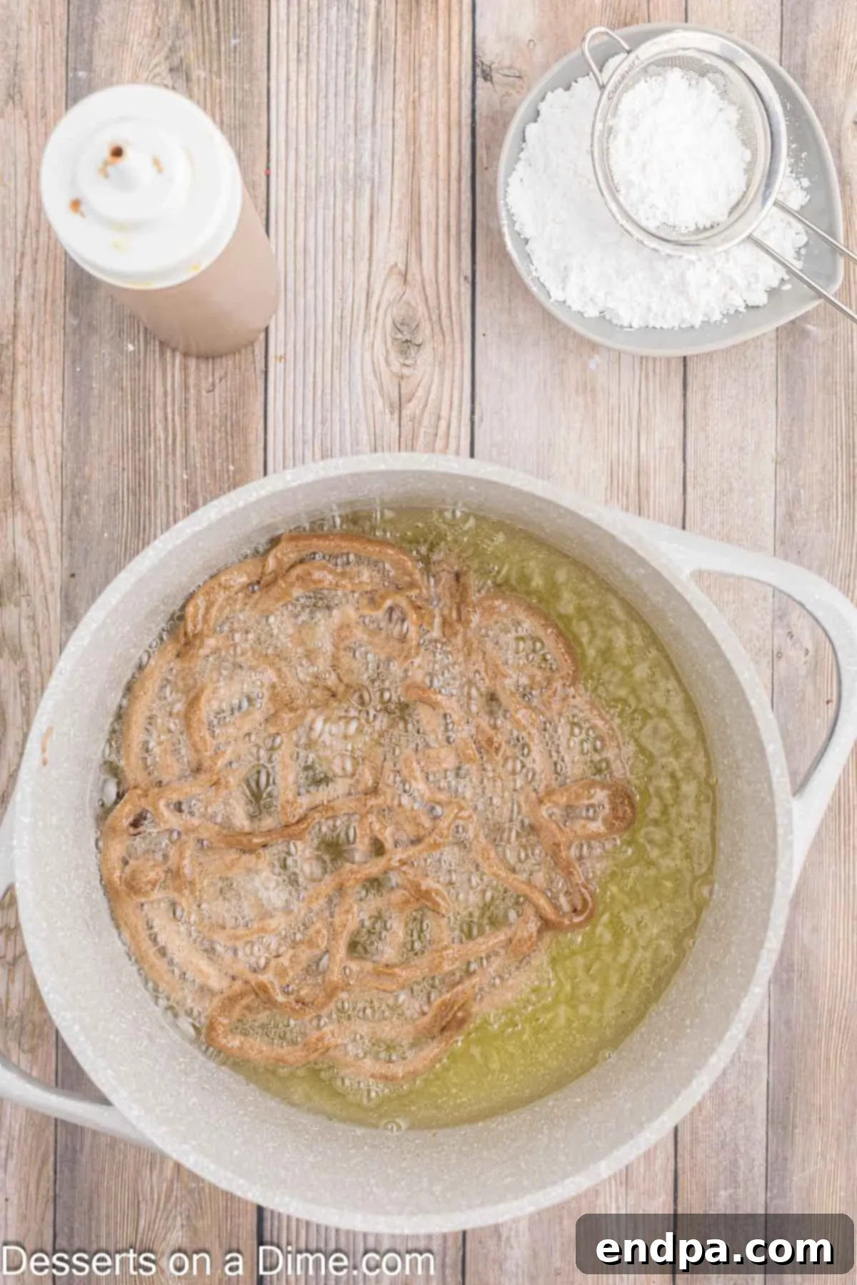 Chocolate funnel cake batter being drizzled and frying in hot oil, forming its signature criss-cross pattern.