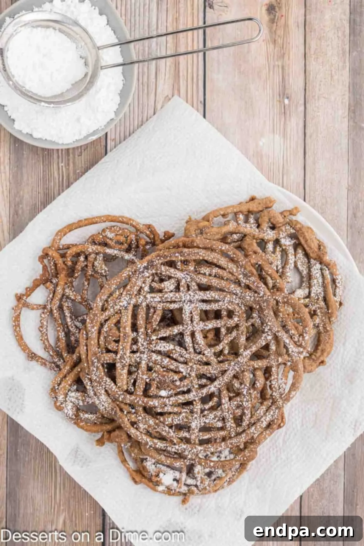 A freshly fried chocolate funnel cake placed on a paper towel-lined plate to drain excess oil.