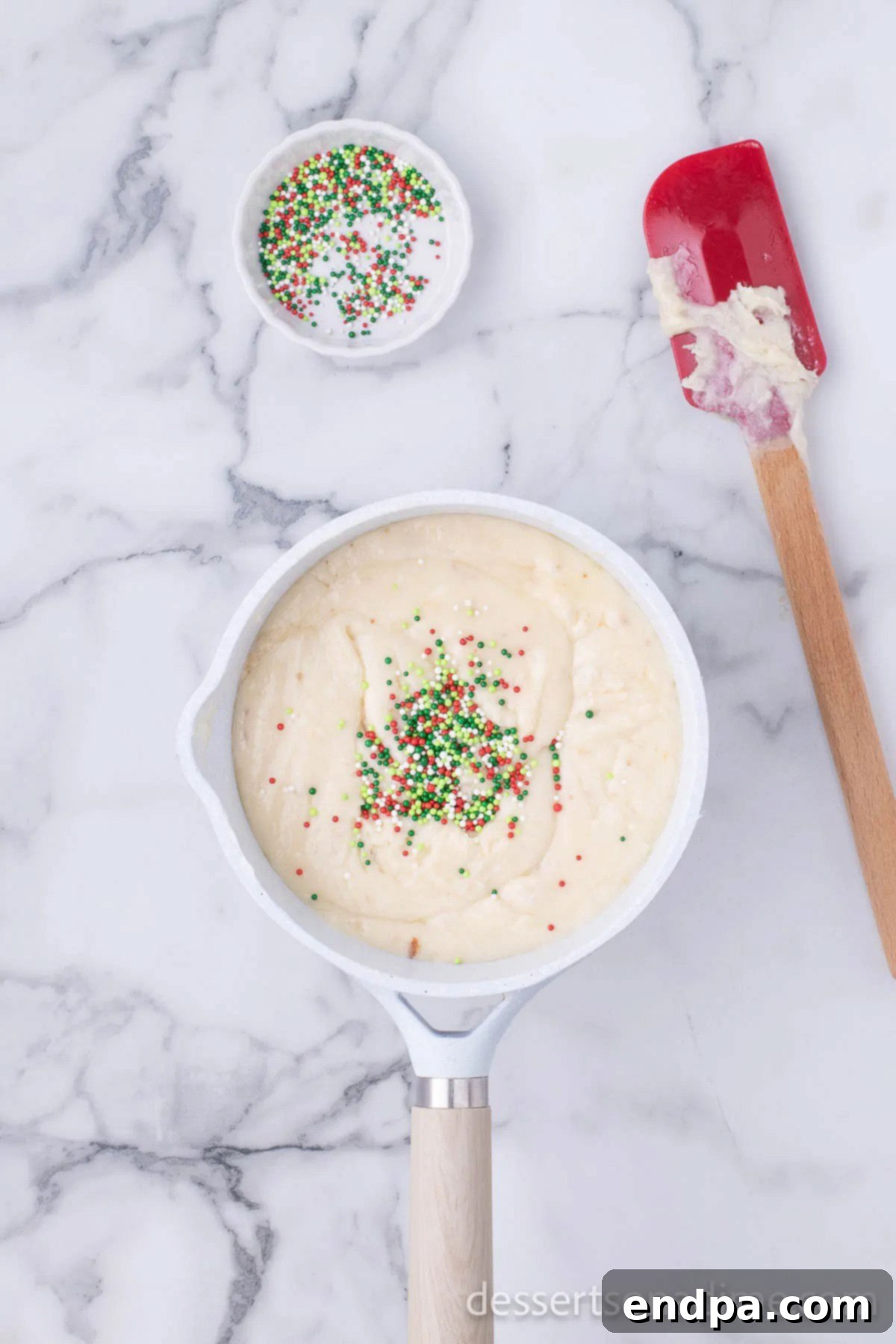 Half of the red, green, and white Christmas sprinkles being gently mixed into the warm white chocolate fudge base.