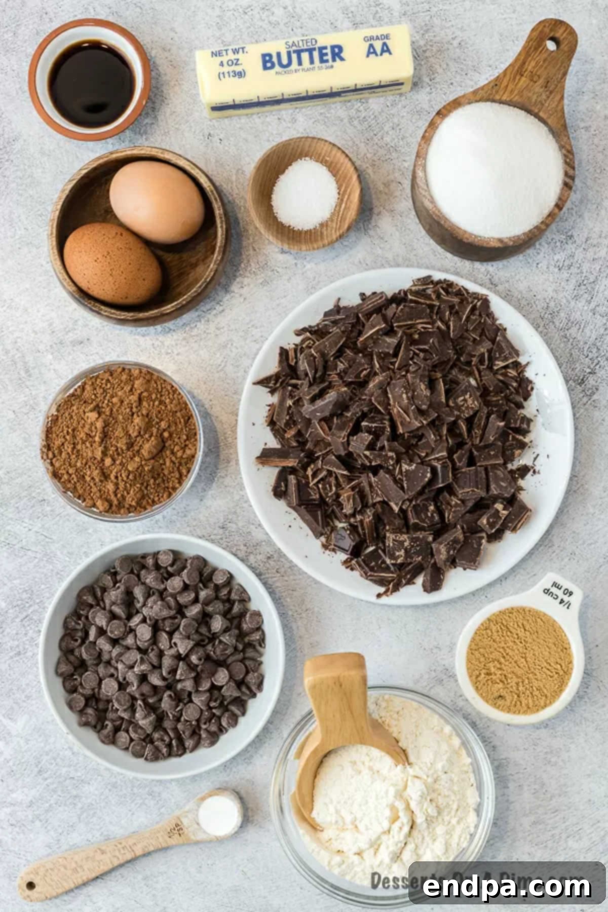 Various ingredients for brownie cookies laid out, including flour, cocoa powder, chocolate, butter, eggs, brown sugar, and vanilla extract.