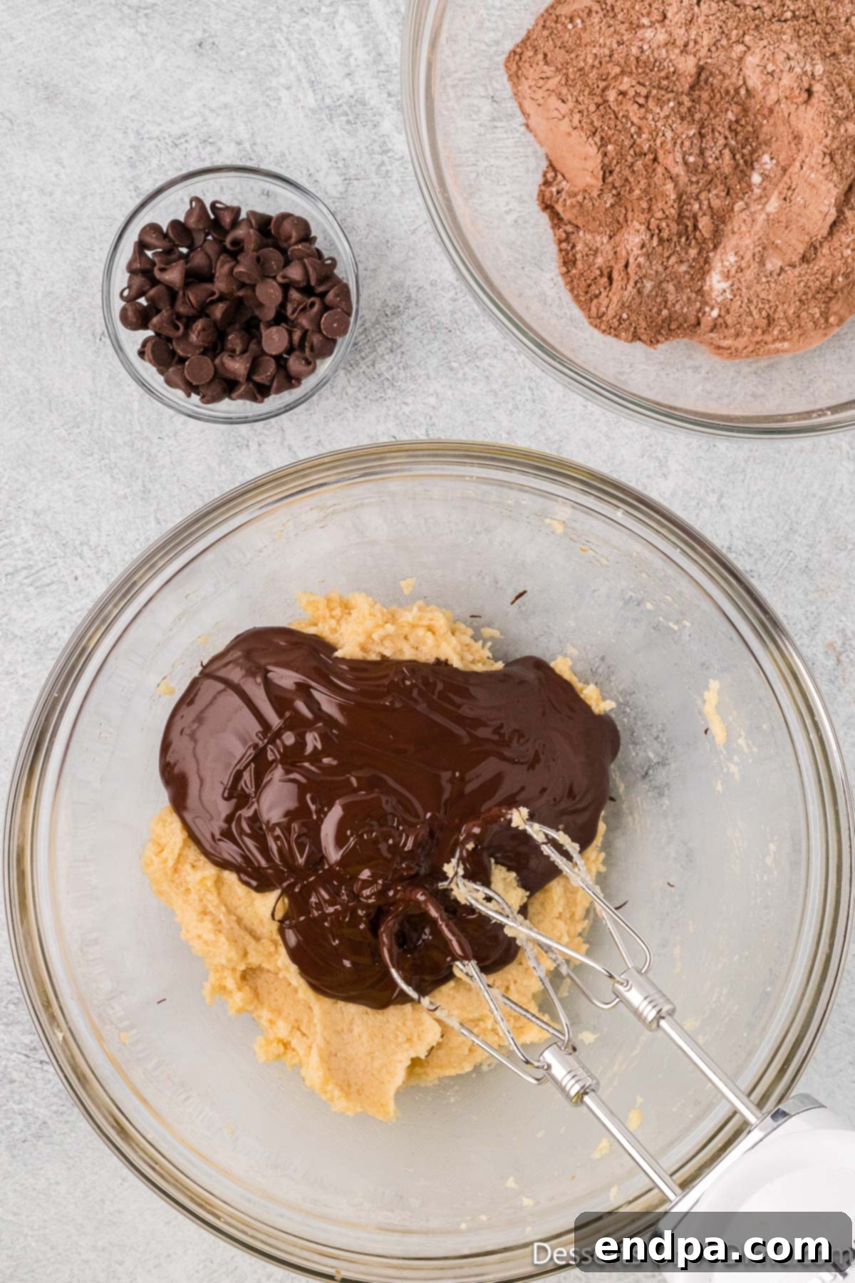 Cooled melted chocolate being poured into the creamy butter and sugar mixture.