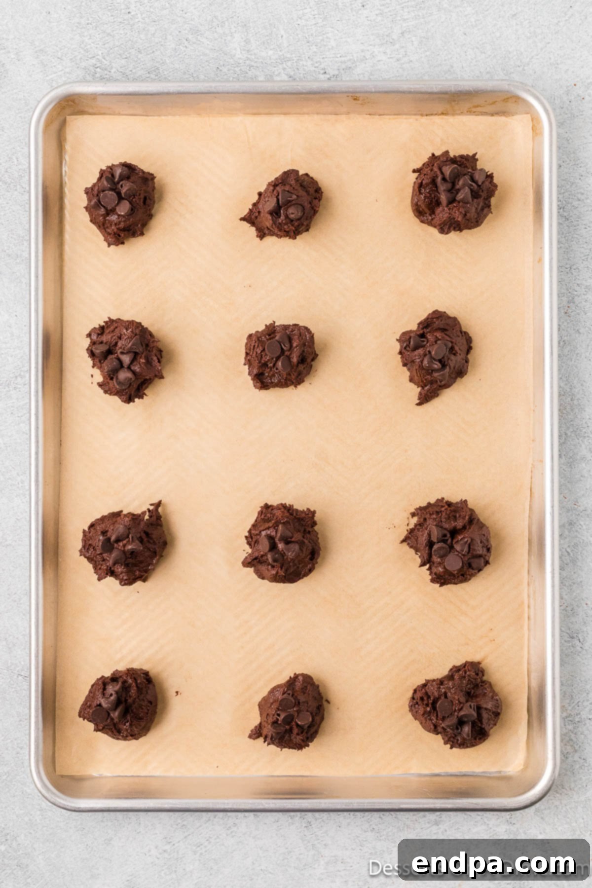 Scoops of brownie cookie dough placed neatly on a parchment-lined cookie sheet.