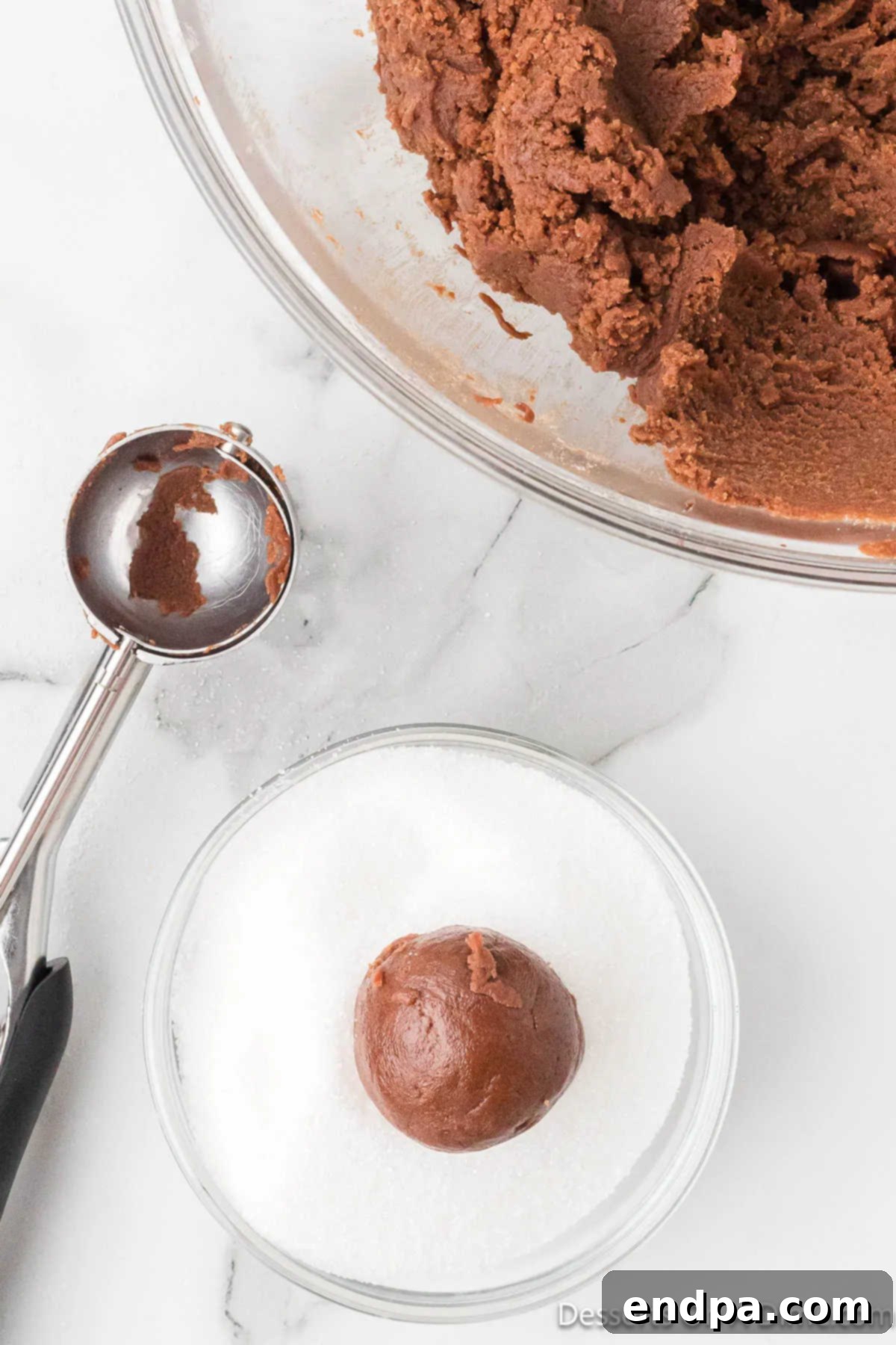Cookie dough balls are dipped and rolled in a bowl of granulated sugar, coating them completely.
