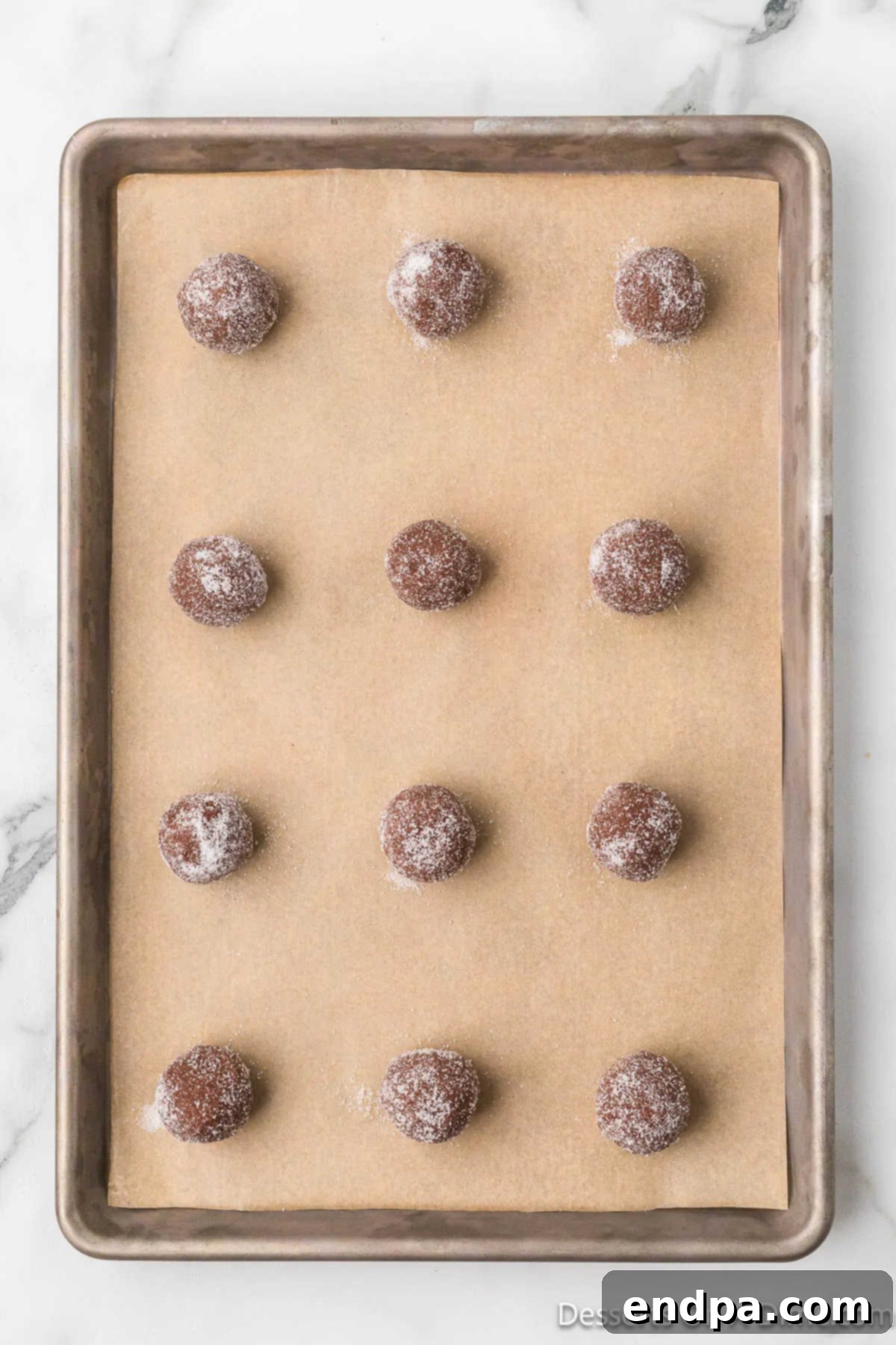 Sugared cookie dough balls are neatly placed on a baking sheet lined with parchment paper, spaced several inches apart.