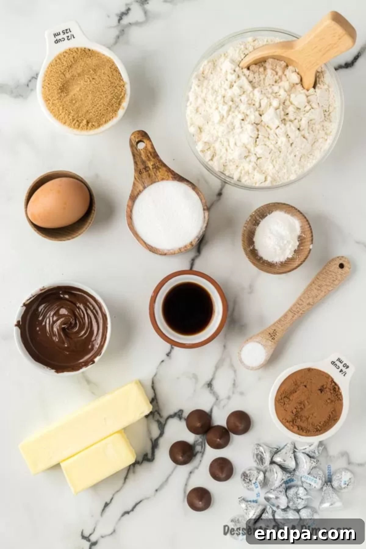 A flat lay photograph showcasing all the essential ingredients required for making chocolate kiss cookies, including softened butter, granulated sugar, brown sugar, vanilla extract, a large egg, all-purpose flour, unsweetened cocoa powder, semi-sweet baking chocolate, and Hershey's Kisses.