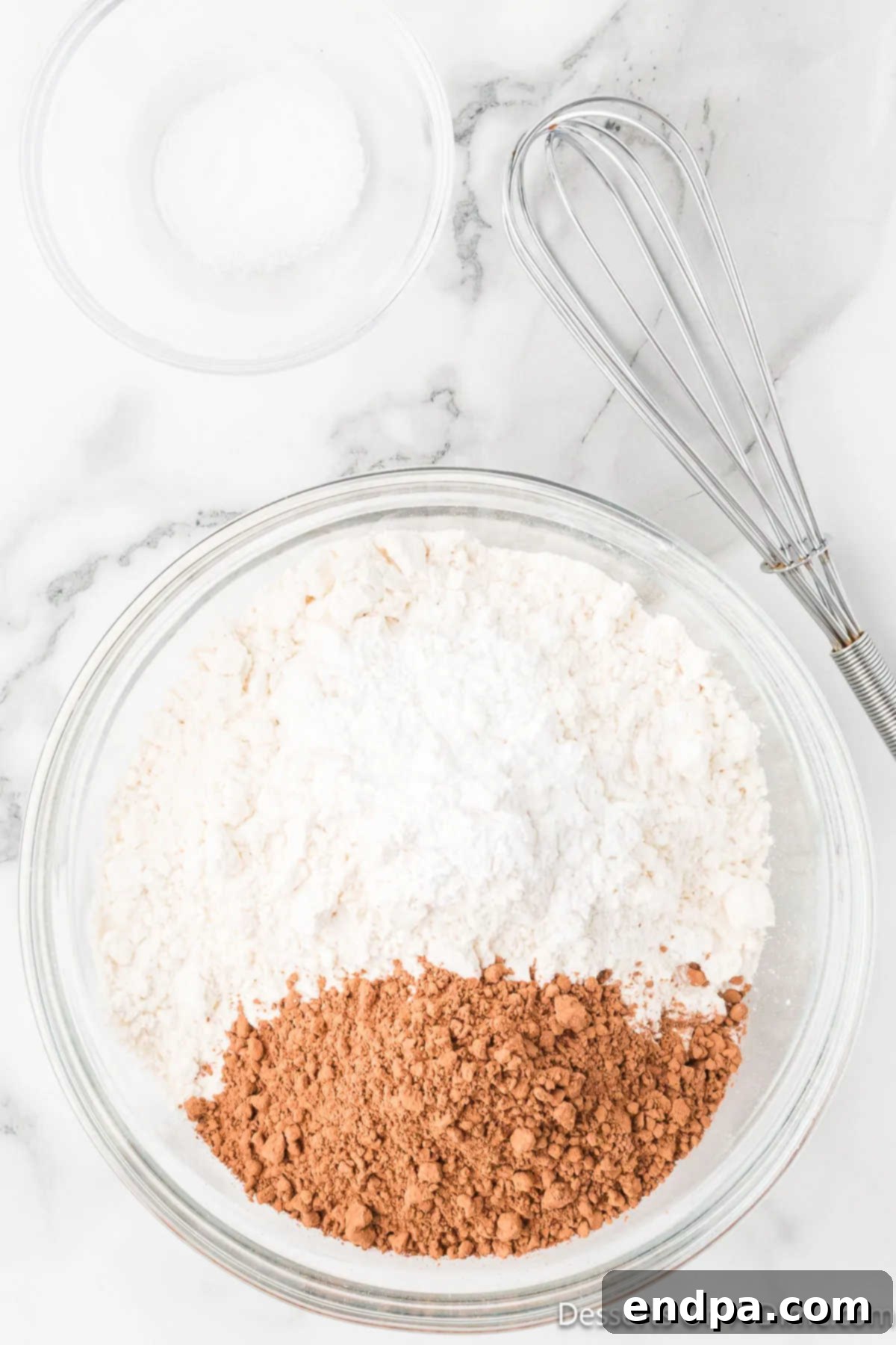 A separate mixing bowl contains all-purpose flour, cocoa powder, baking powder, and salt, combined and ready to be whisked.