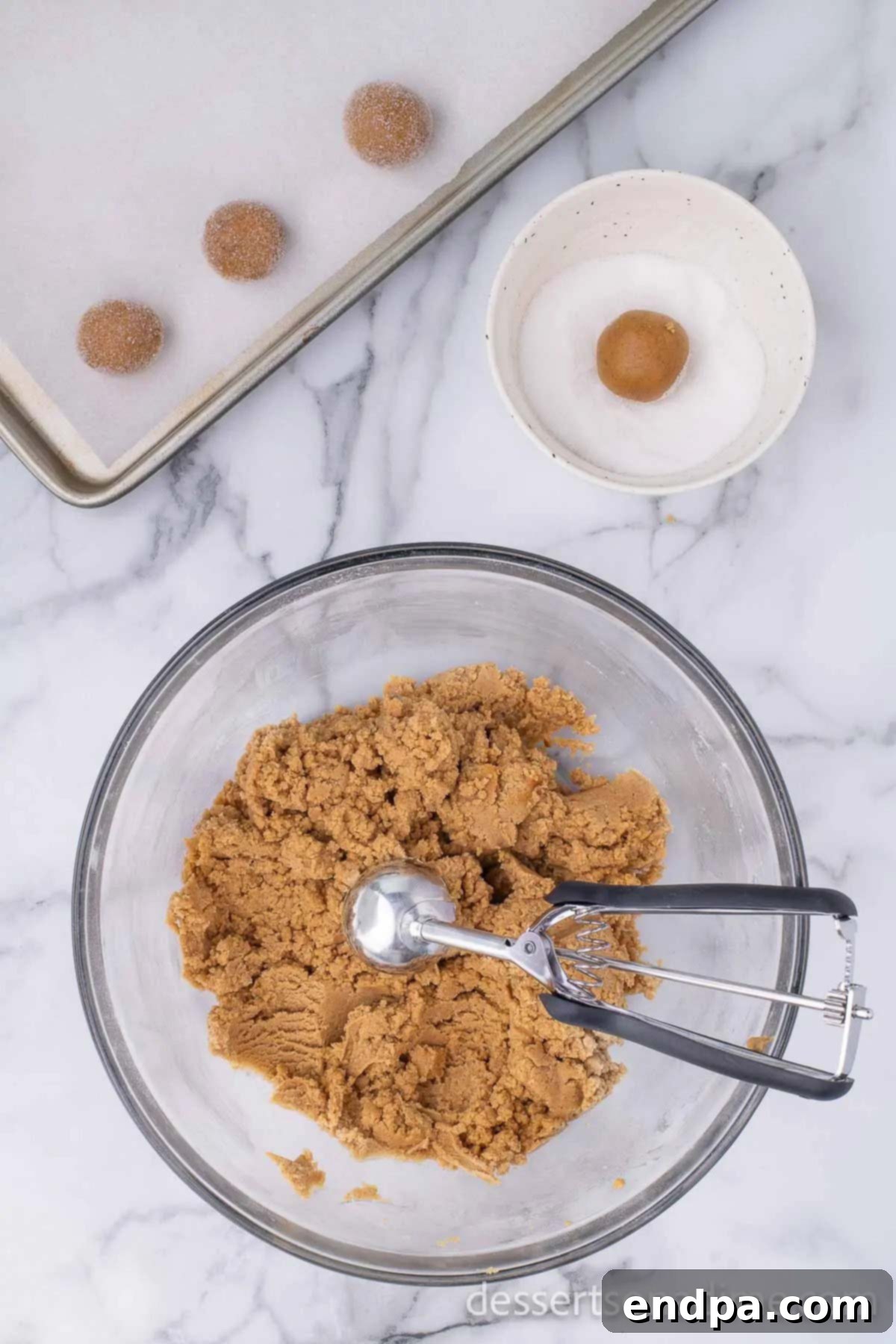 Cookie dough being scooped into uniform balls and rolled in sugar.
