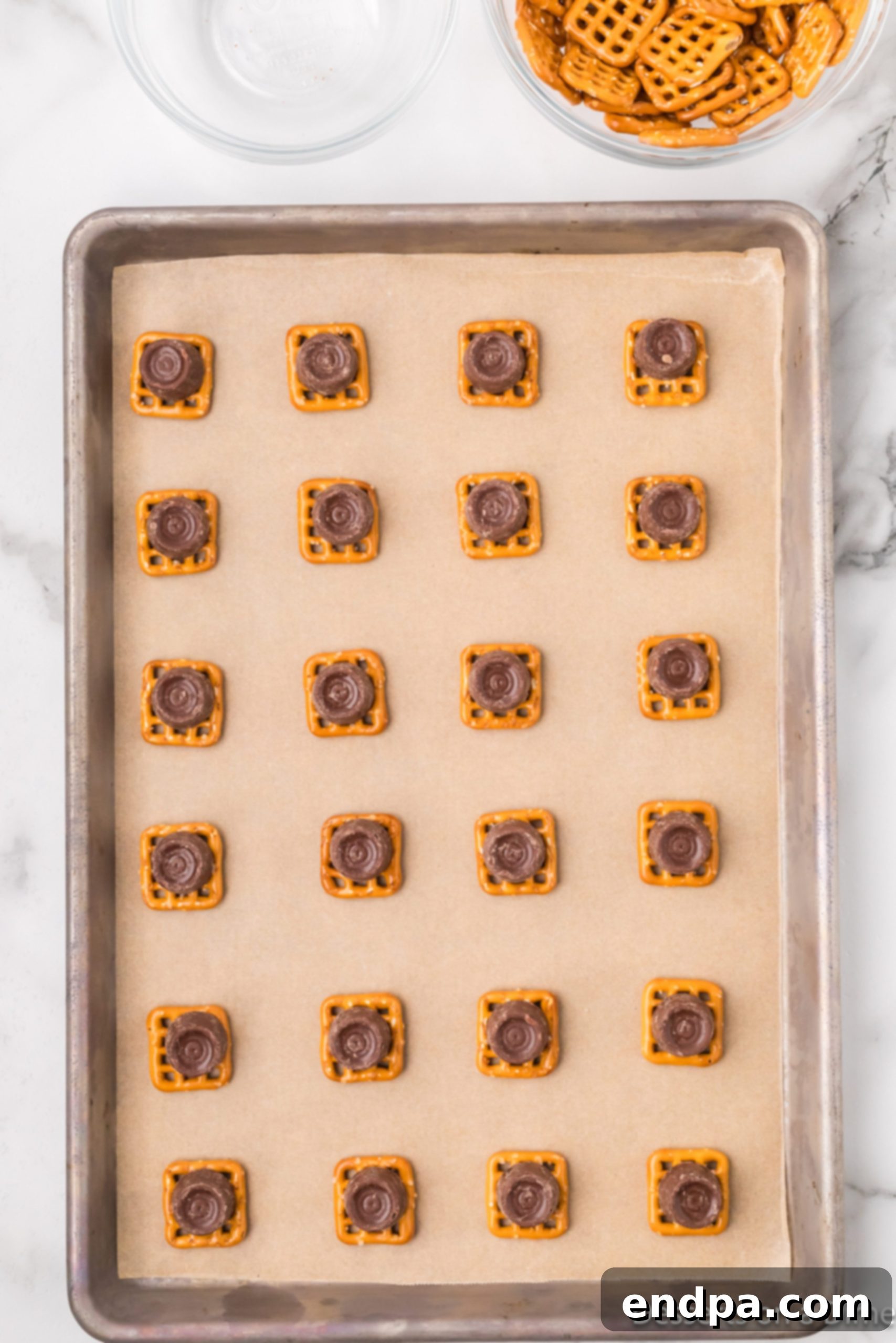 Unwrapped Rolo candy placed on top of each pretzel on a baking sheet.
