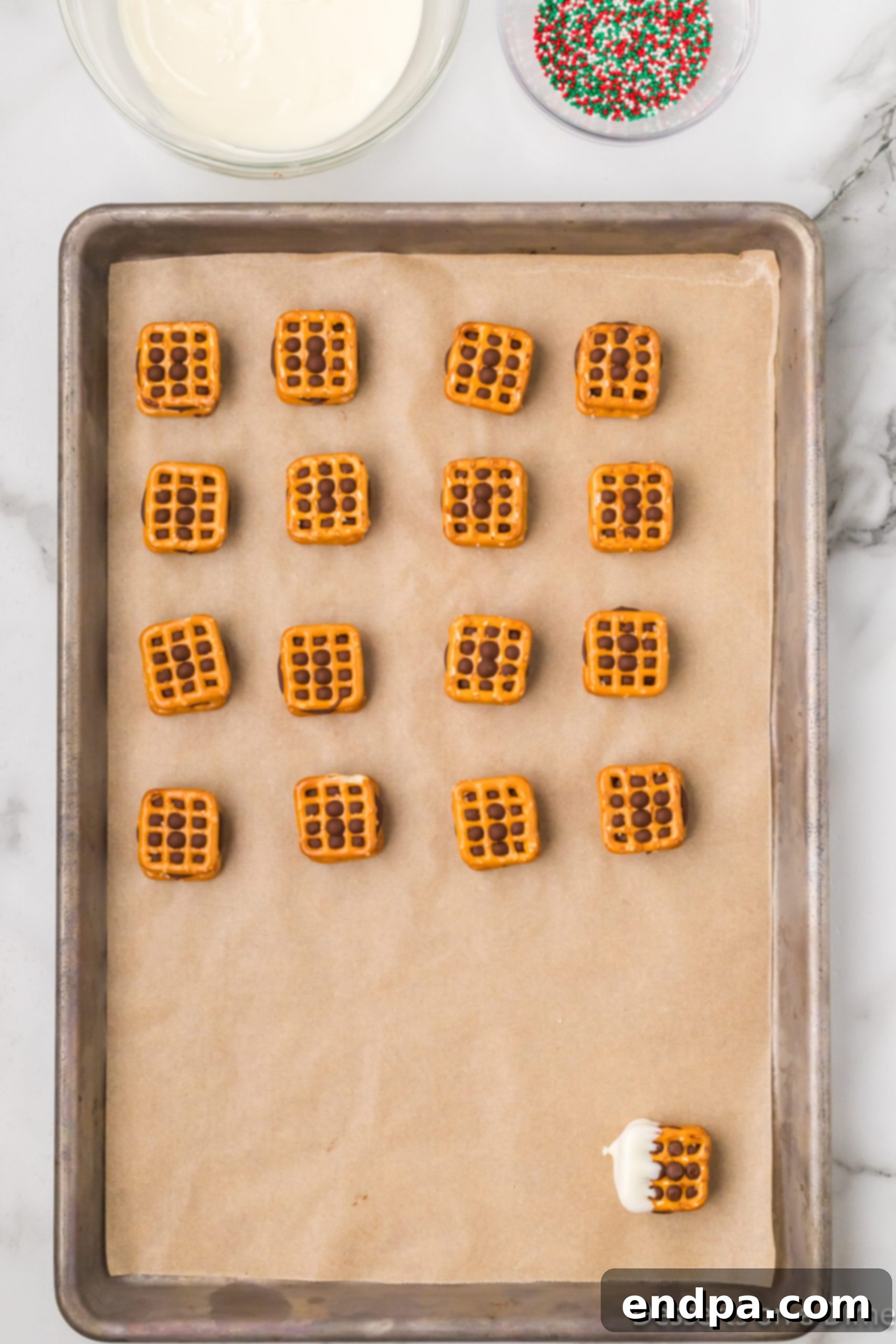 Rolo Pretzel Sandwiches partially dipped in white chocolate, laid out on parchment paper.