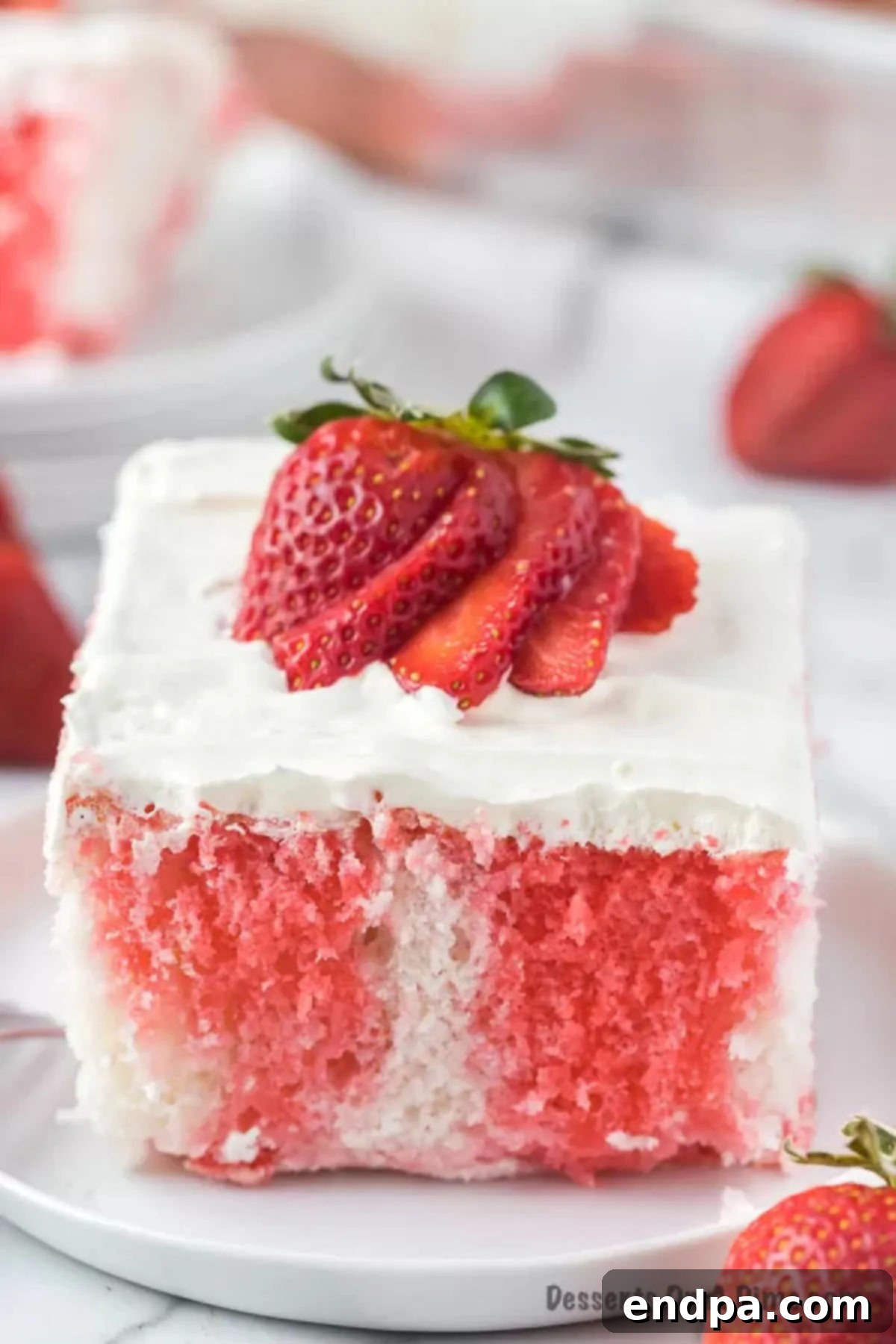 A slice of Strawberry Poke Cake on a plate, showcasing its layers and fresh strawberry topping.