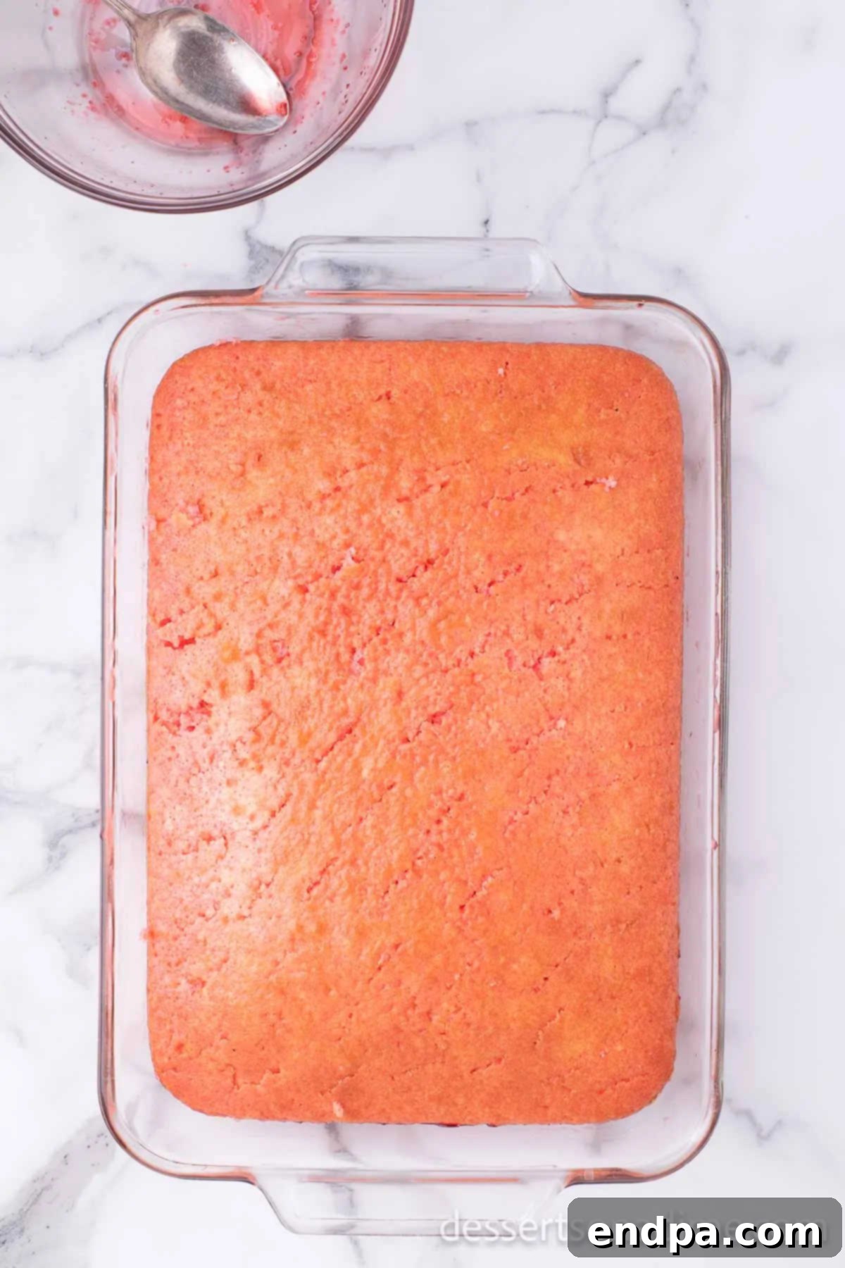 Strawberry Jello mixture being poured evenly over the poked cake.