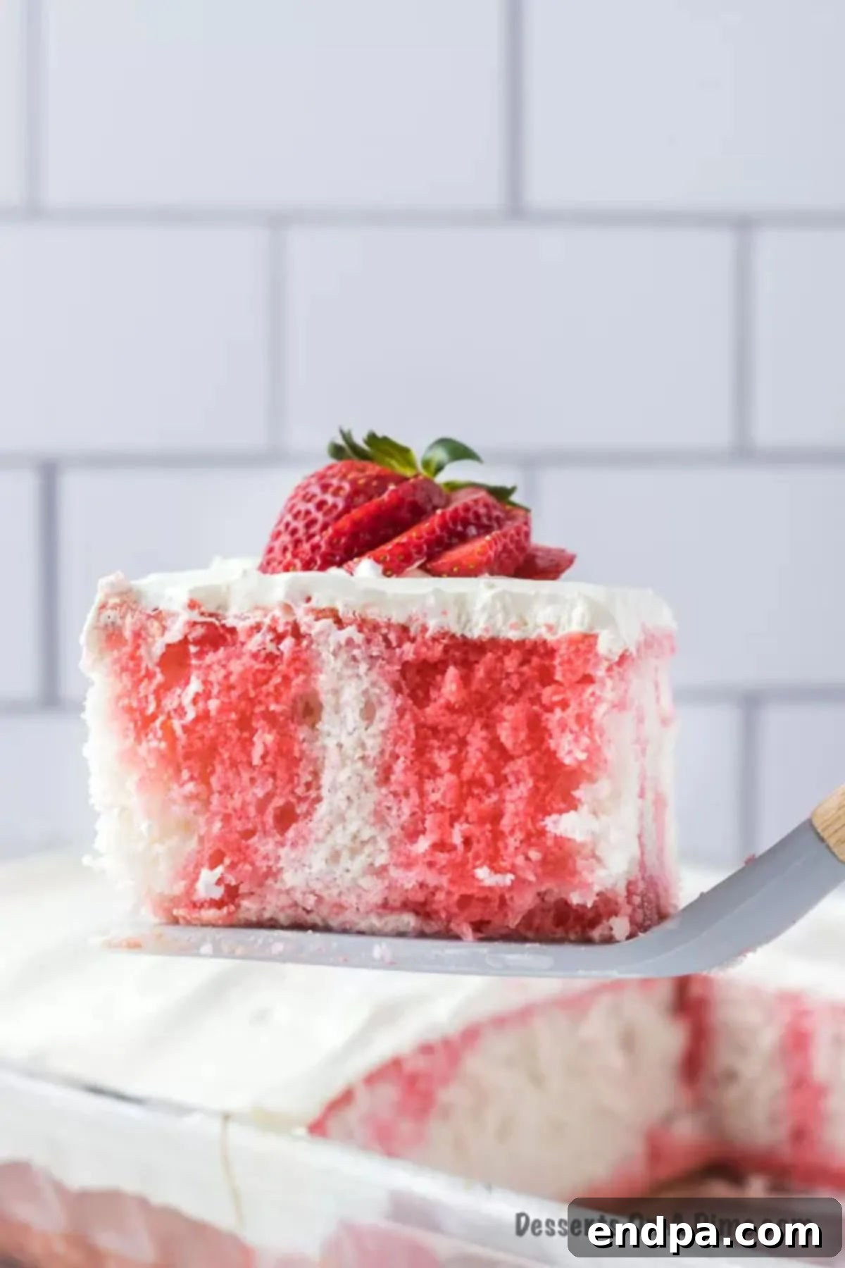 A perfectly sliced piece of Strawberry Poke Cake being lifted with a spatula.