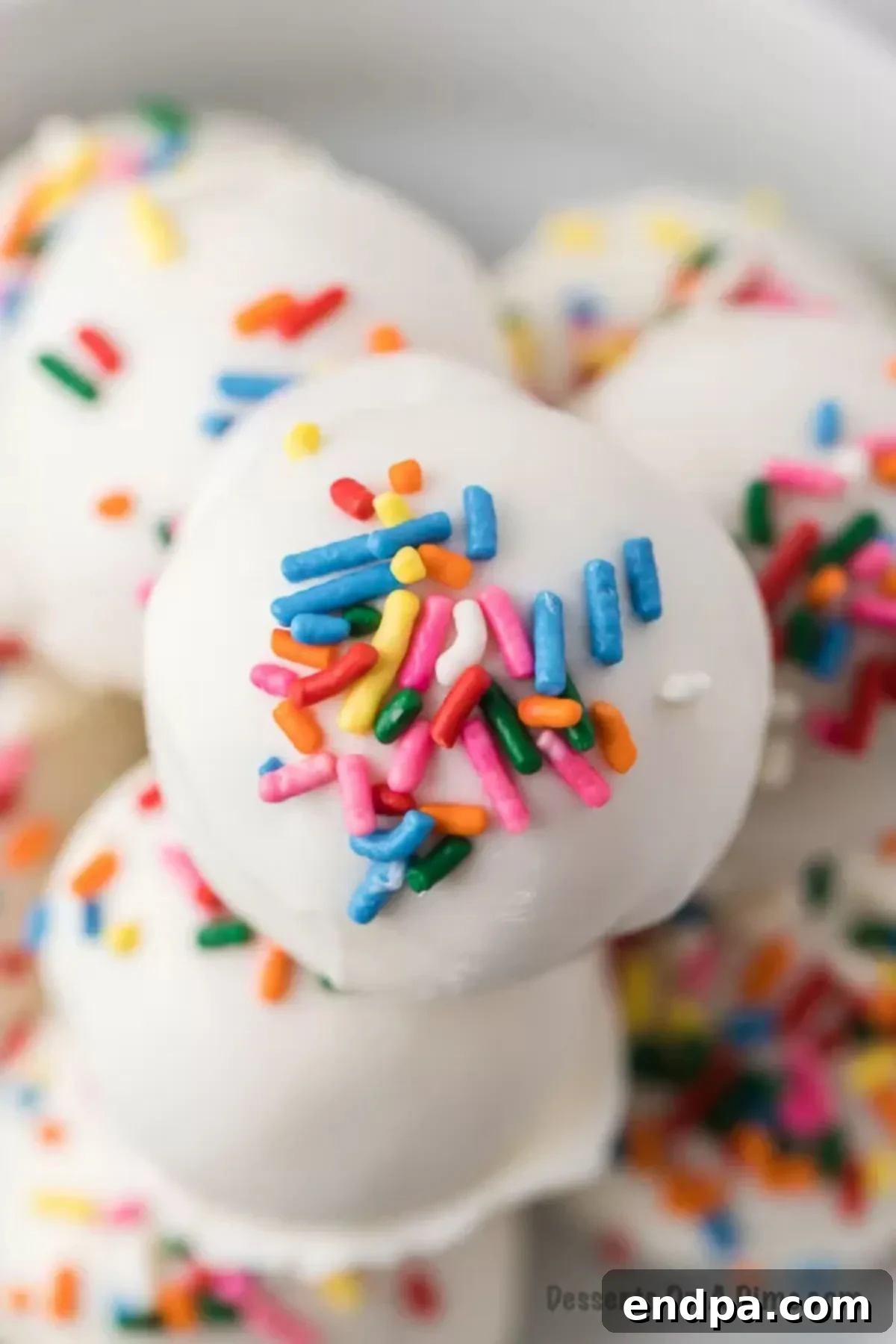 Cake balls arranged together with colorful sprinkles on a white surface.