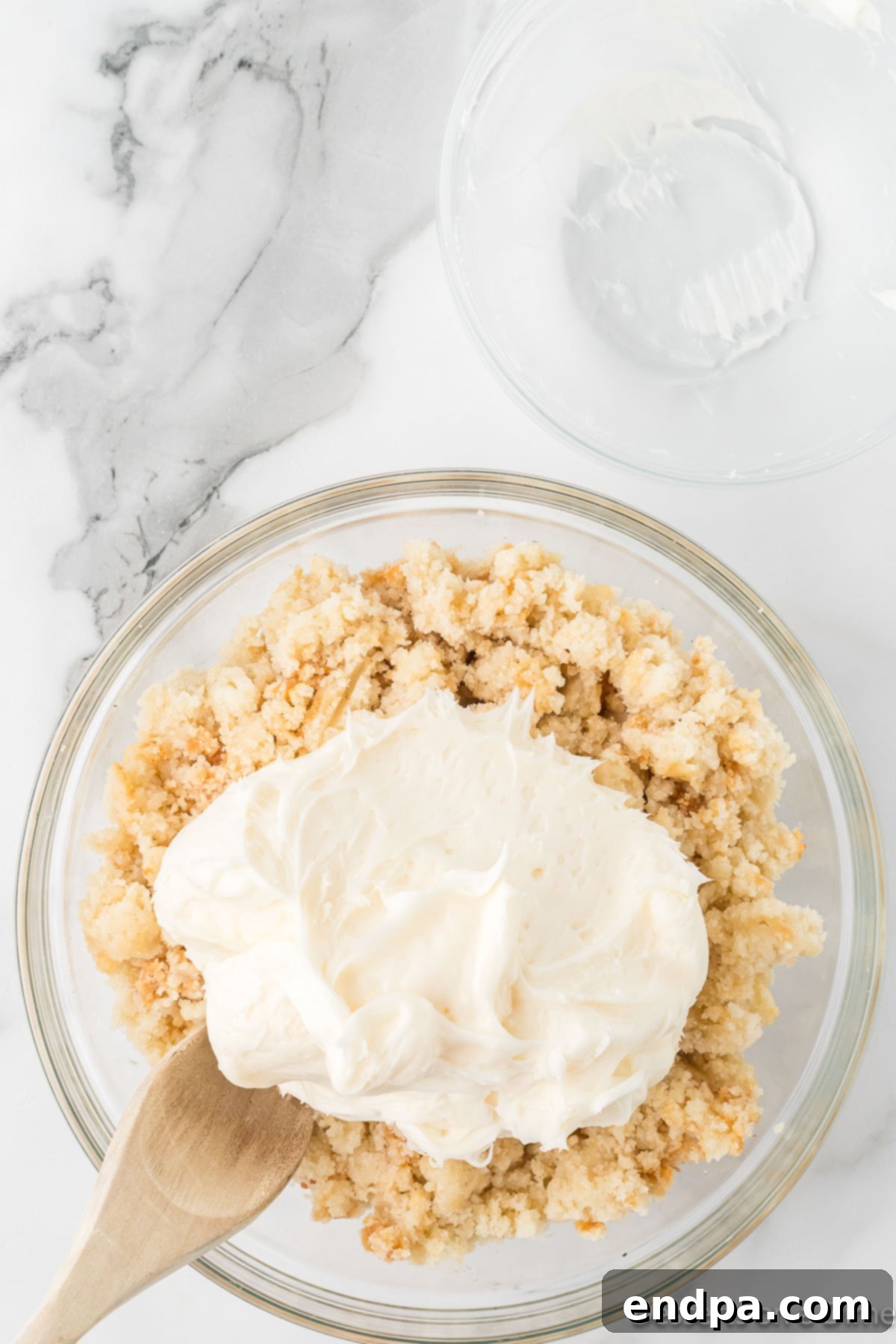 Crumbled cake in a mixing bowl with a scoop of frosting on top.