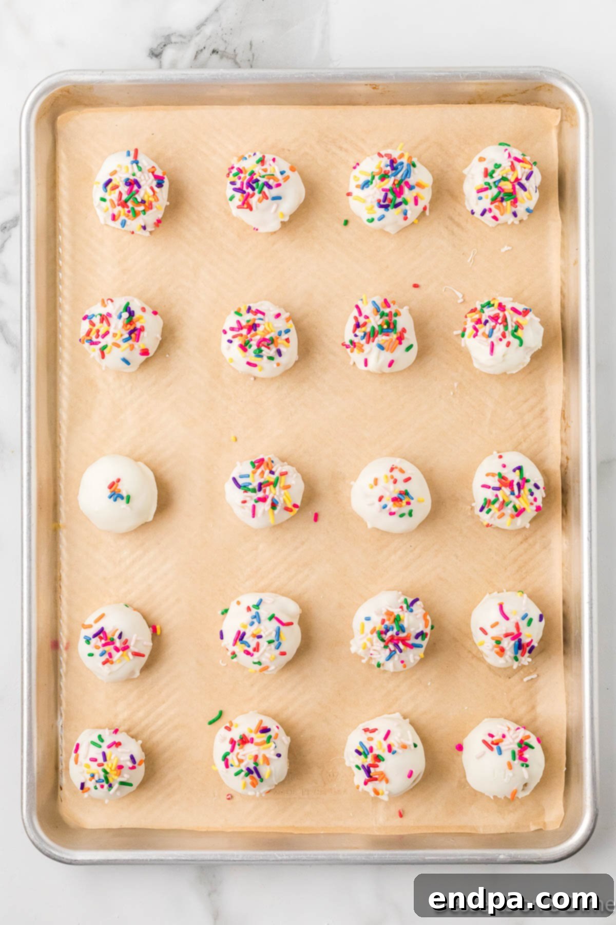Coated and sprinkled vanilla cake balls cooling on a parchment-lined baking sheet.