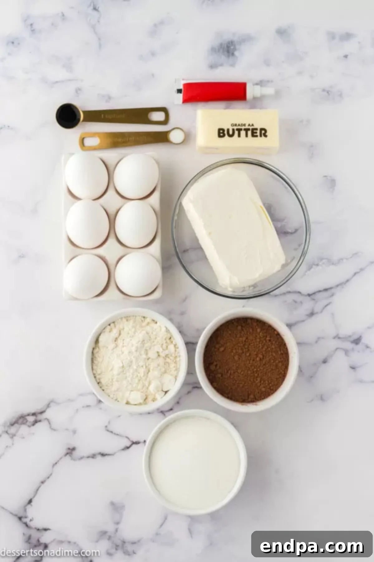 Swirled Red Velvet Cheesecake Brownies 3 Ingredients for Red velvet cheesecake brownies - cocoa powder, red food coloring, cream cheese, eggs, milk, flour, sugar, and vanilla extract are laid out on a table.