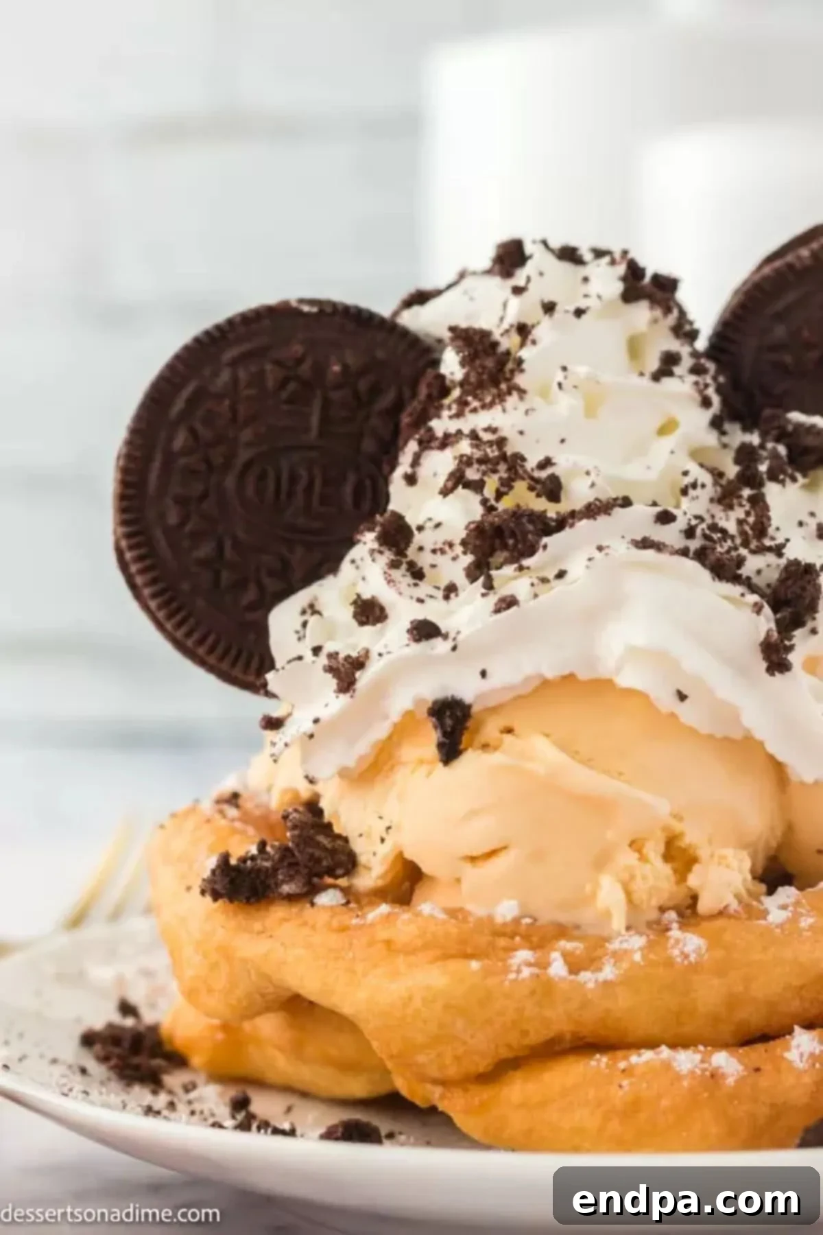 Up close photo of Oreo funnel cake on a plate, richly topped with ice cream, whipped cream, and crushed Oreos.