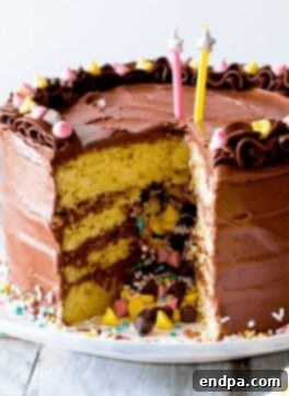 A slice of Piñata Cake revealing a colorful candy surprise inside, with fudge frosting.