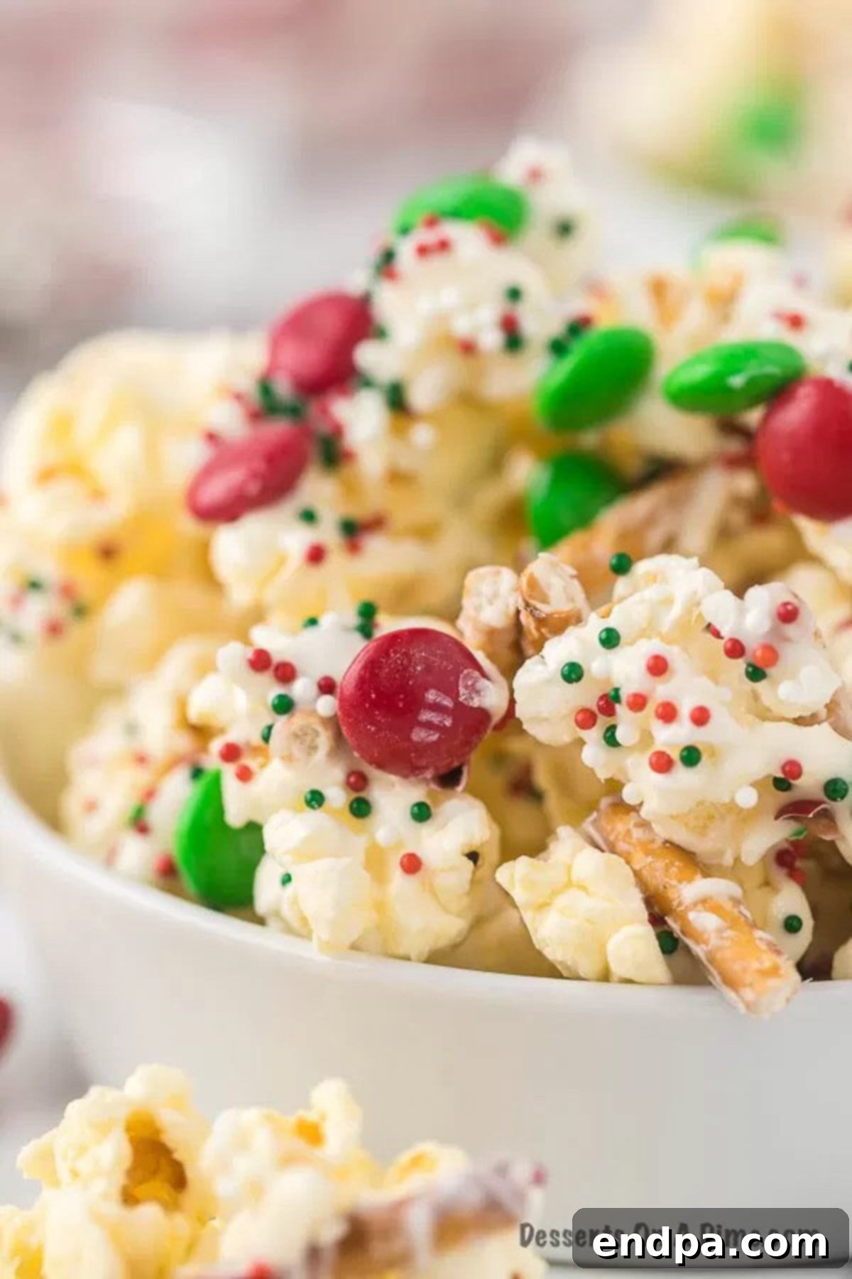 A bowl filled with festive Christmas Crunch, featuring white chocolate-covered popcorn, pretzels, red and green M&Ms, and colorful sprinkles.