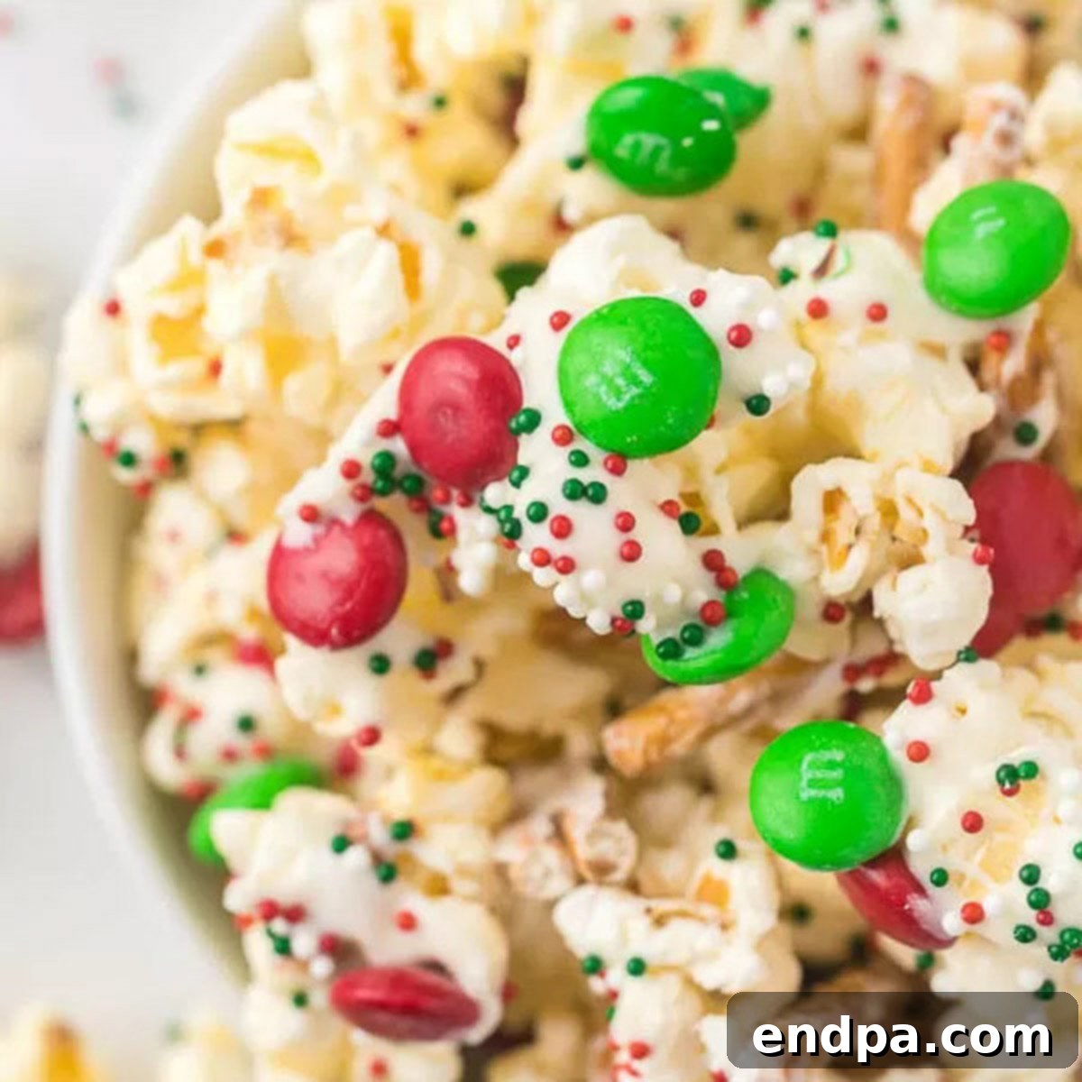 Close-up of a festive Christmas Crunch snack in a bowl, showcasing the white chocolate, pretzels, M&Ms, and sprinkles.