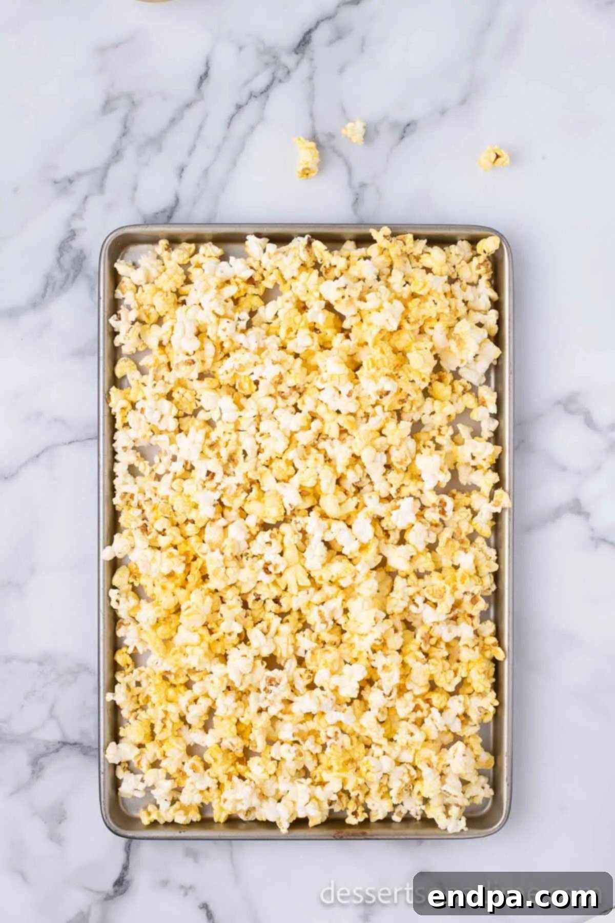 Freshly popped popcorn spread evenly on a baking sheet lined with parchment paper.