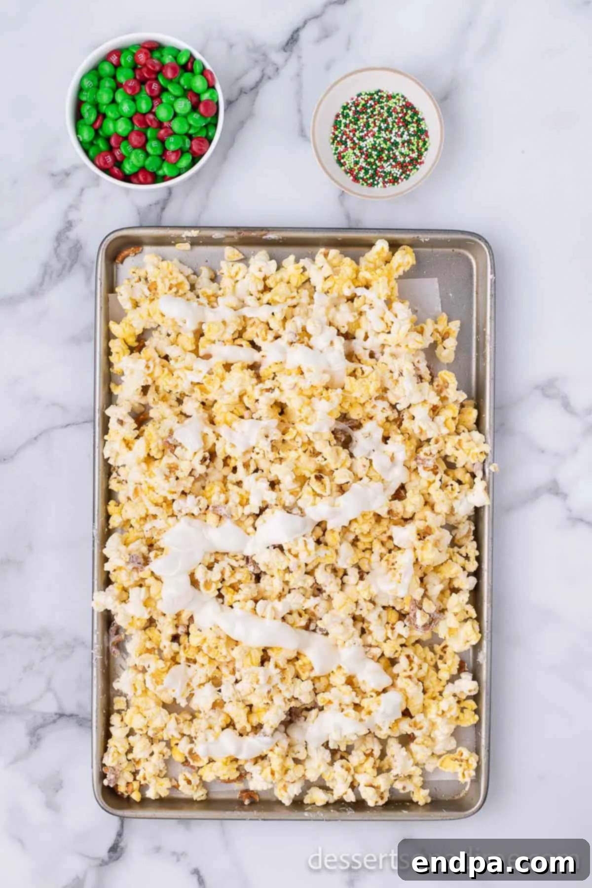 Remaining melted white chocolate drizzled over the partially coated popcorn mixture.