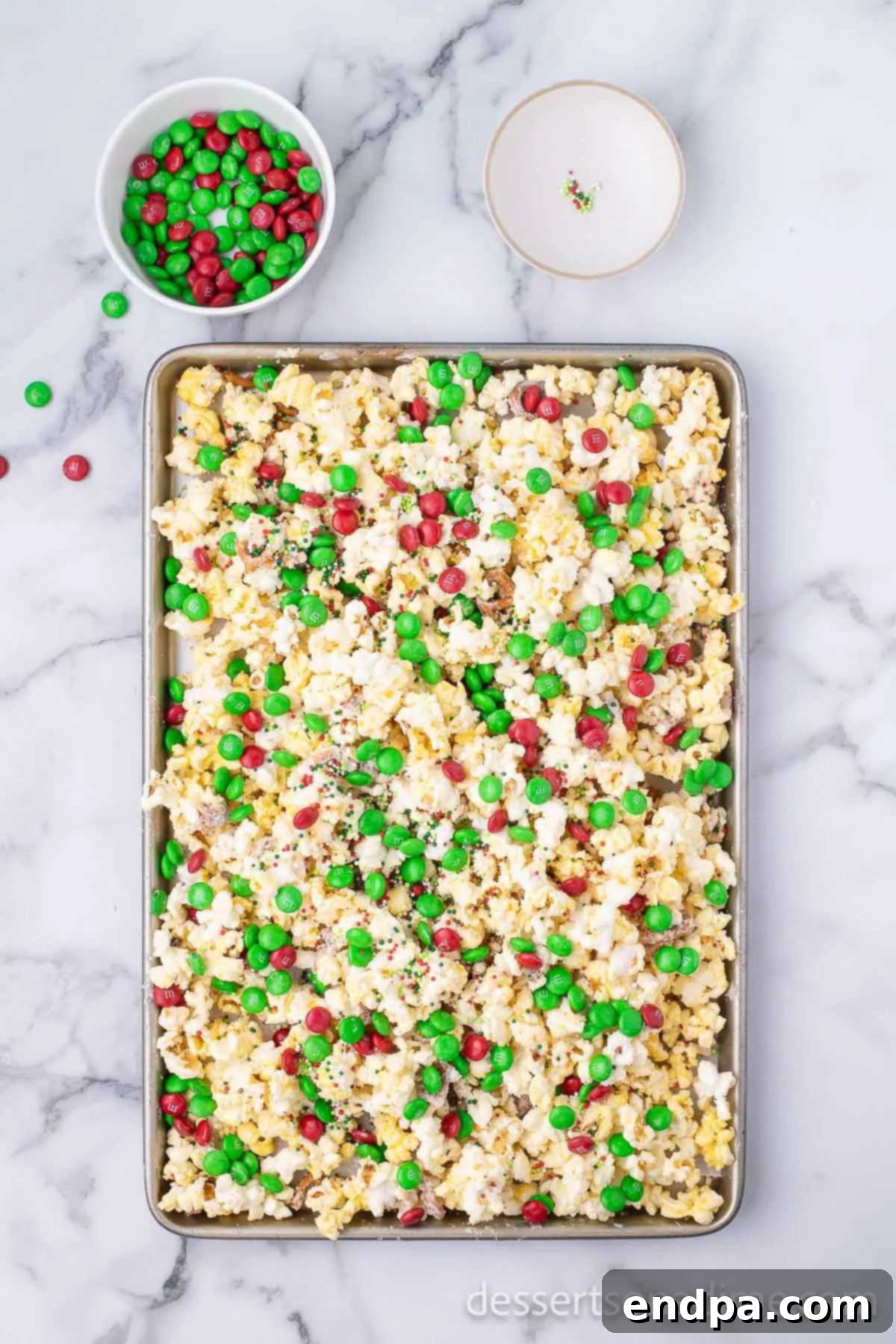 Red and green M&Ms and festive sprinkles generously applied to the white chocolate-coated popcorn mixture.