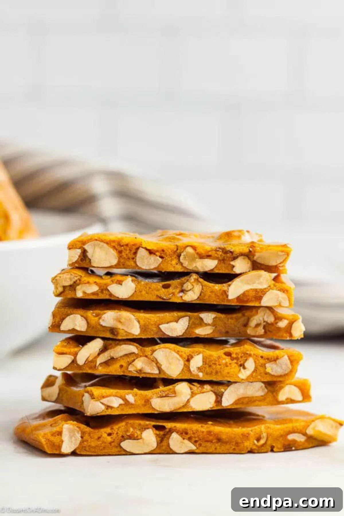 Stacked pieces of golden microwave peanut brittle with whole peanuts visible.
