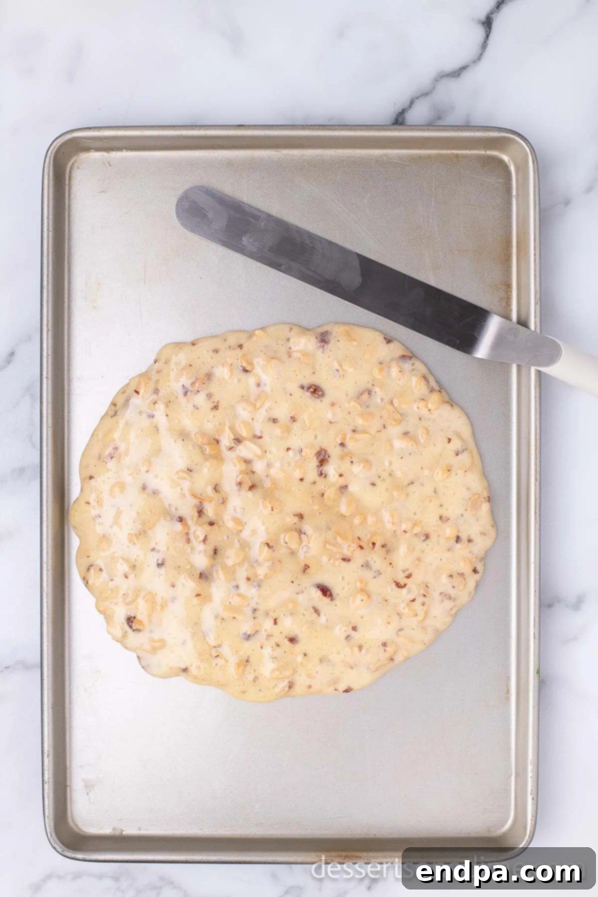 Hot peanut brittle mixture being poured onto a buttered baking sheet.