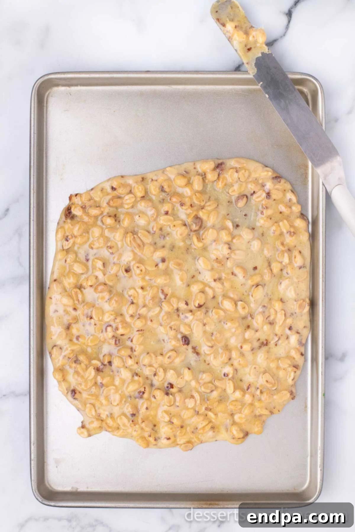 Spreading the hot peanut brittle mixture thinly on a cookie sheet with a spatula.
