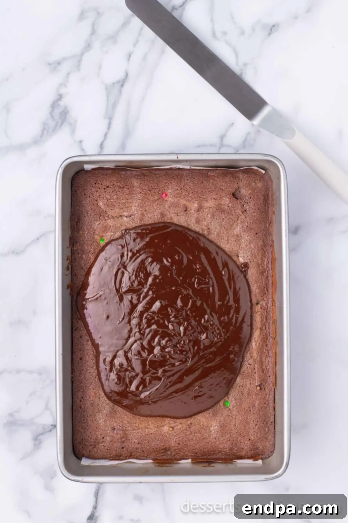 Merry & Bright Brownies 10 Chocolate ganache being spread evenly over the warm brownies with a spatula.
