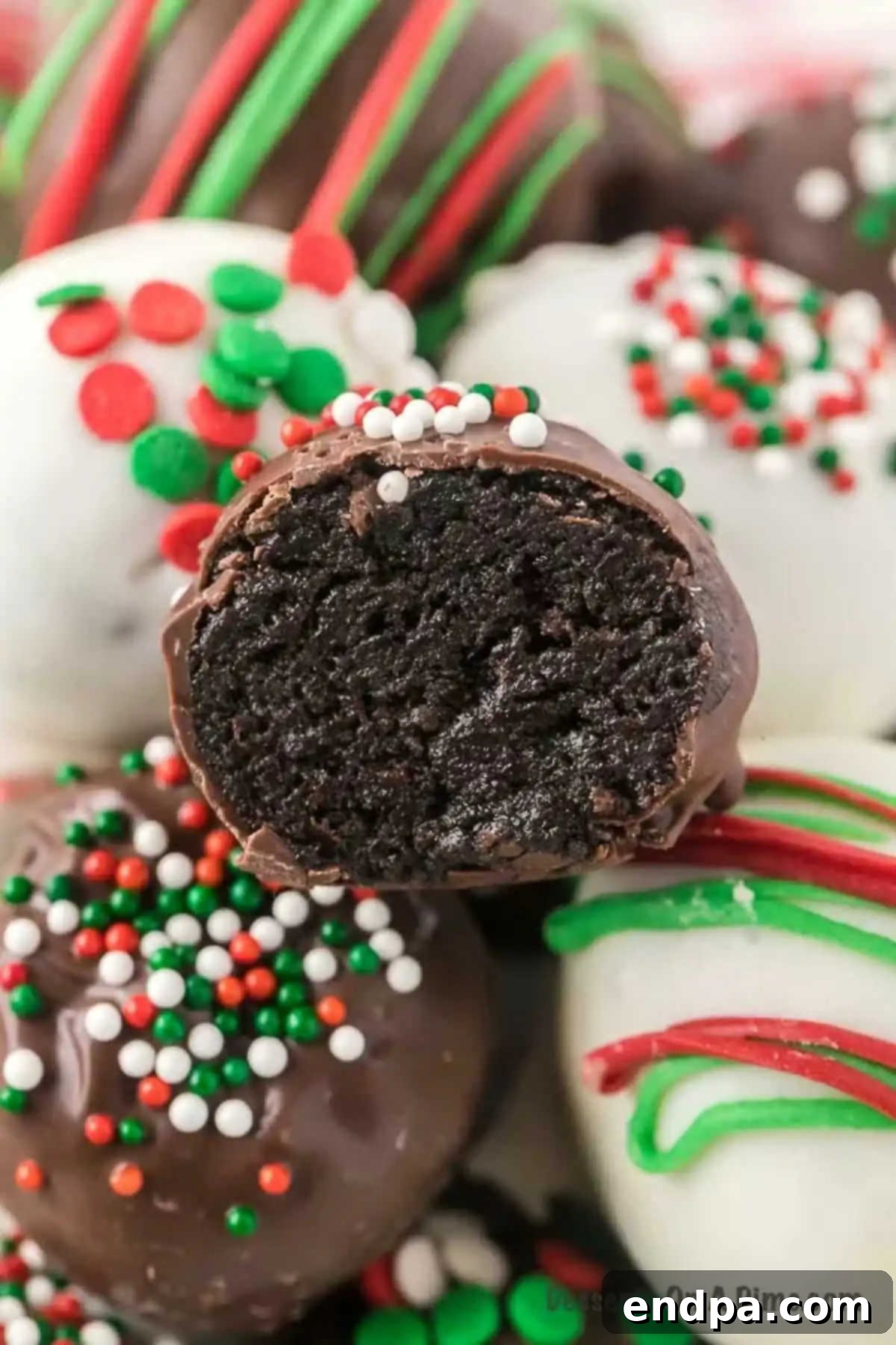 Irresistible Holiday Oreo Truffles 2 A close-up photo of a Christmas Oreo ball cut in half, revealing its creamy, dark cookie-crumb interior, dipped in festive chocolate and adorned with sprinkles.