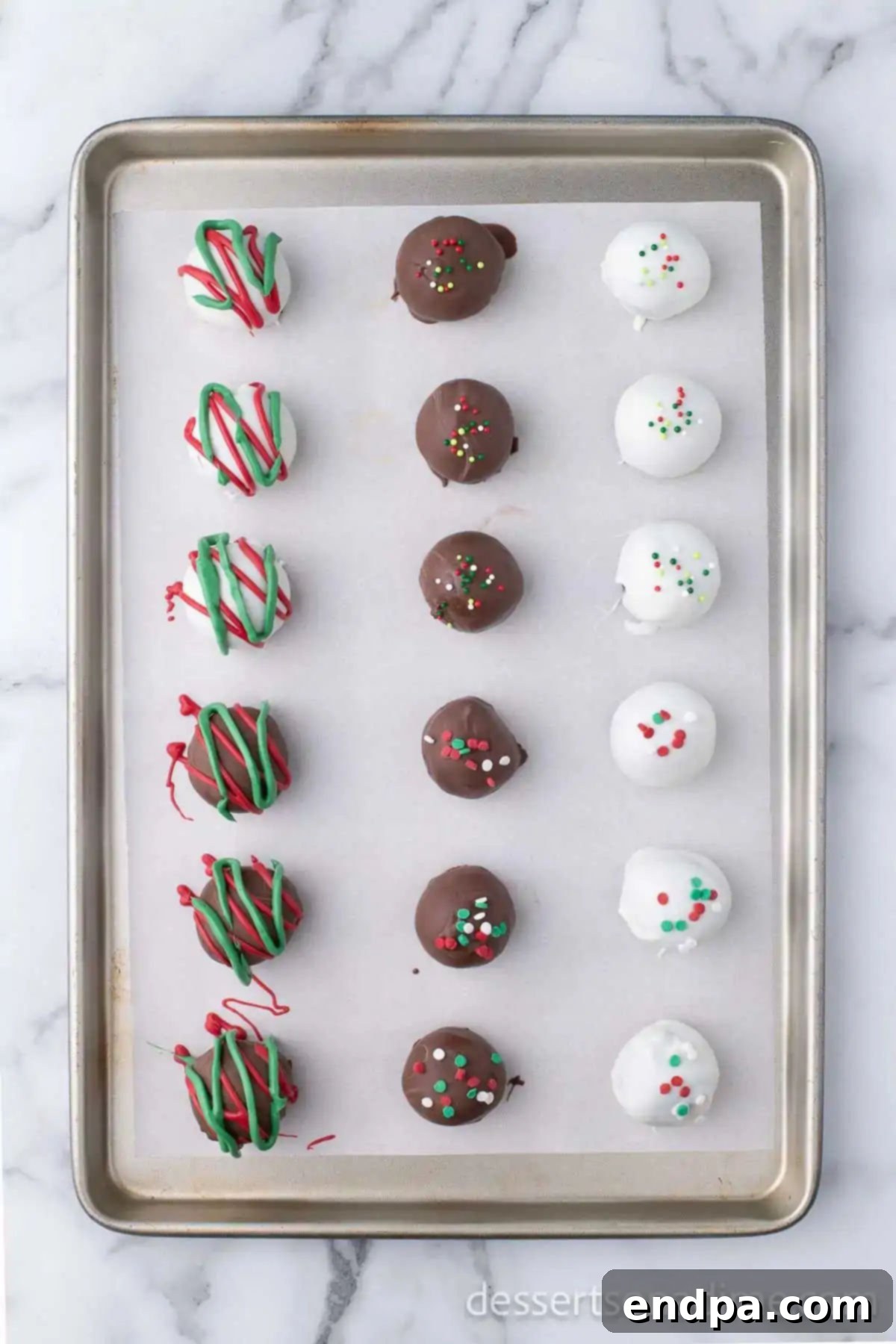 Irresistible Holiday Oreo Truffles 13 A collection of beautifully decorated Christmas Oreo truffles, some with sprinkles and others with colorful drizzles, resting on a baking sheet, waiting to fully set.