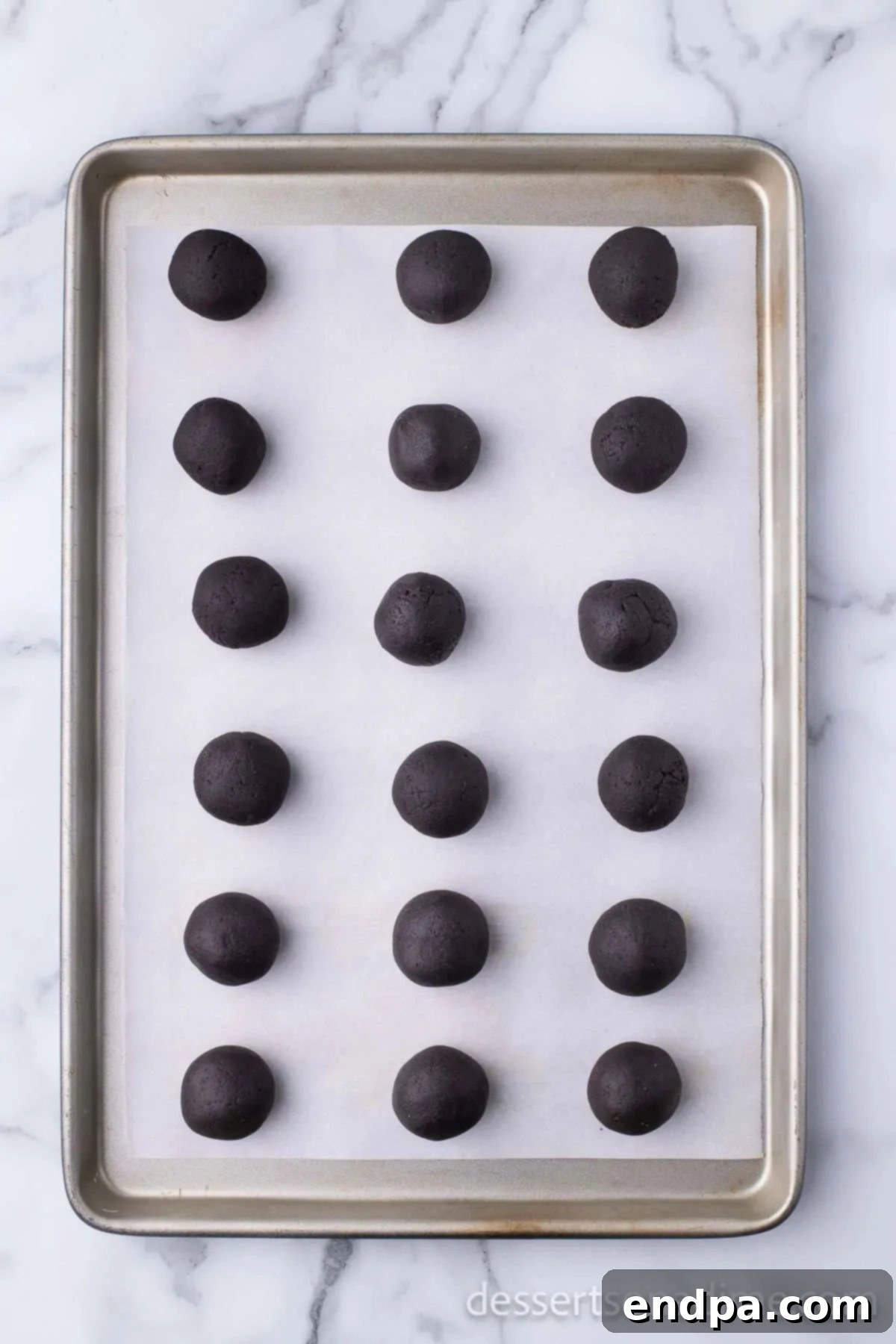 Irresistible Holiday Oreo Truffles 7 Uniformly rolled Oreo balls are neatly arranged on a baking sheet lined with parchment paper, chilling in the freezer.