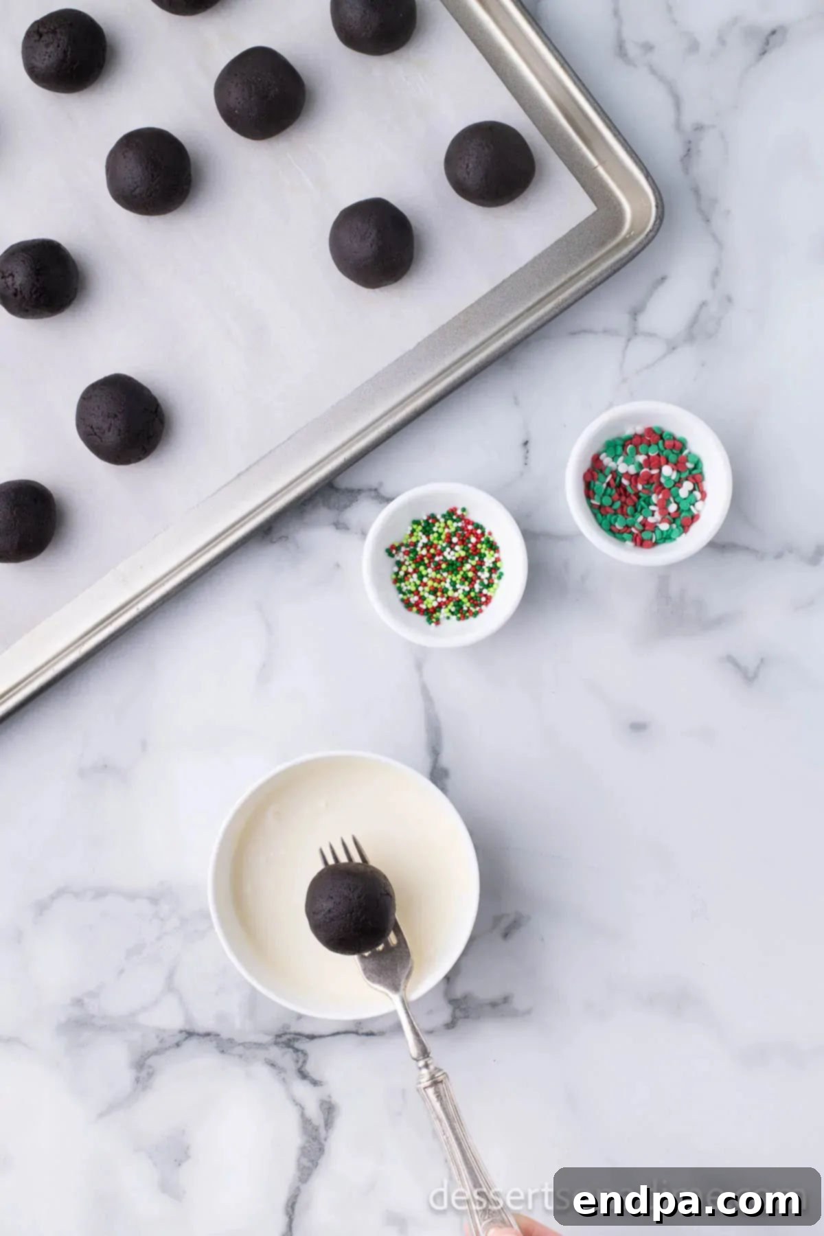 Irresistible Holiday Oreo Truffles 9 An Oreo ball is carefully dipped into melted chocolate using a fork, ensuring a complete and even coating.