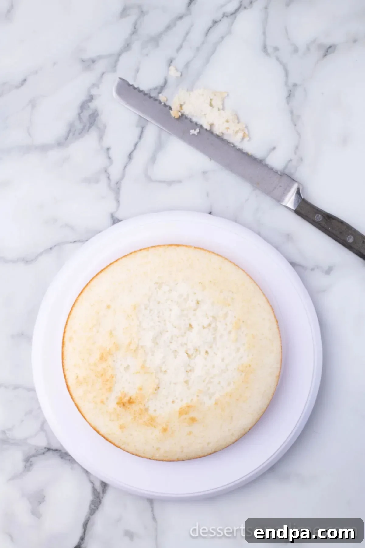 Cake layer being leveled with a serrated knife for even stacking.