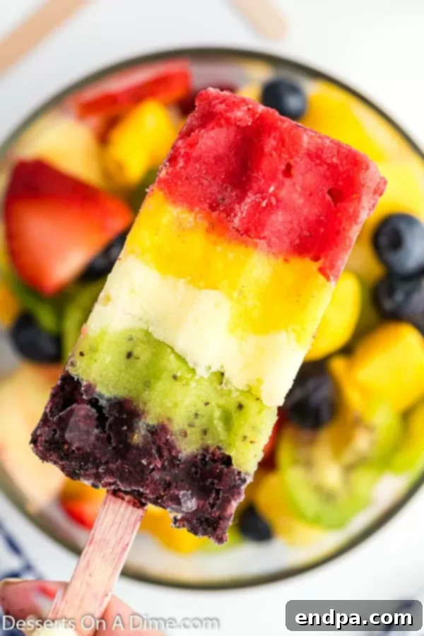 Frozen Rainbow Delights 2 A close-up photo of a vibrant, multi-layered Rainbow Popsicle, showcasing its beautiful blended fruit layers.