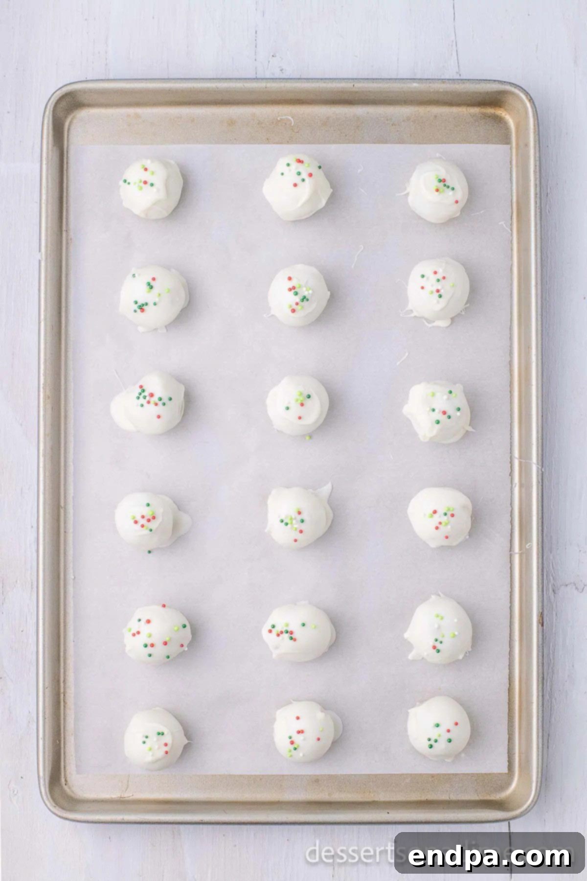 Balls dipped in chocolate and topped with sprinkles sitting on baking sheet. 