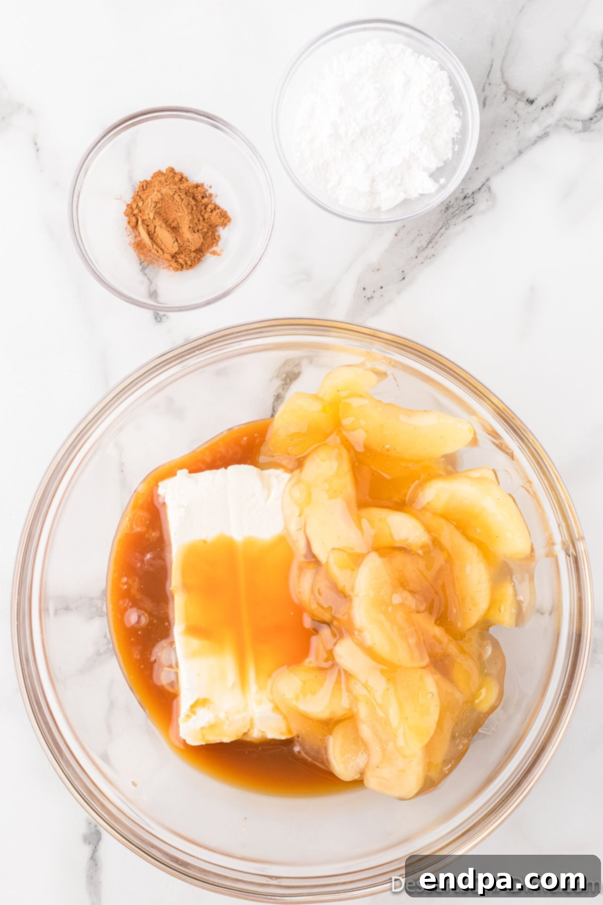 Cream cheese, apples, and caramel sauce in a bowl, before mixing.