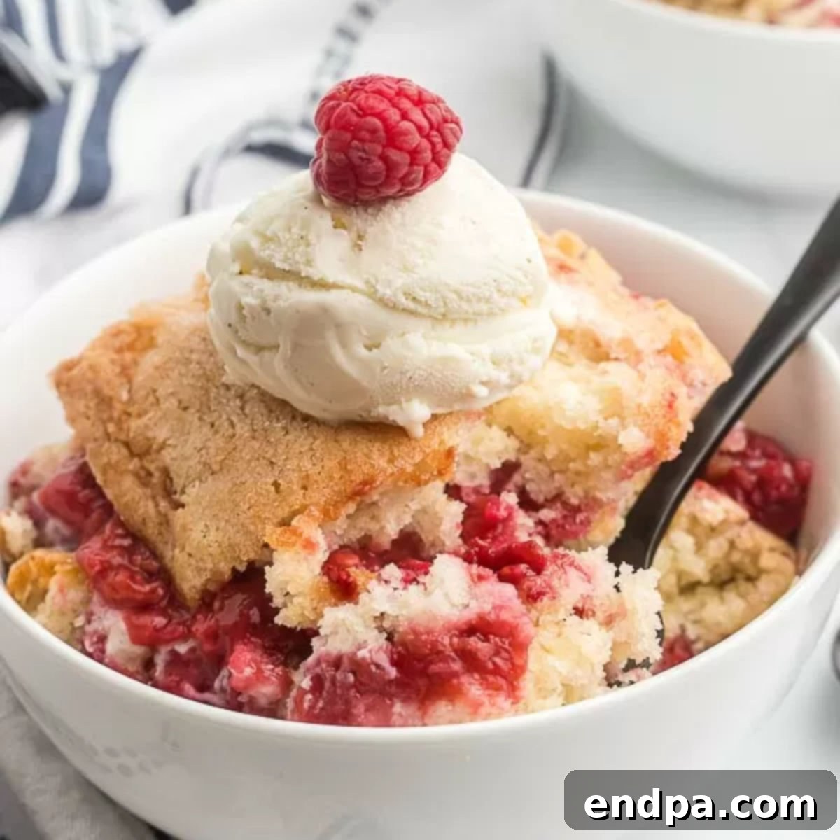 Close-up of a square dish of baked raspberry cobbler with a golden crust.