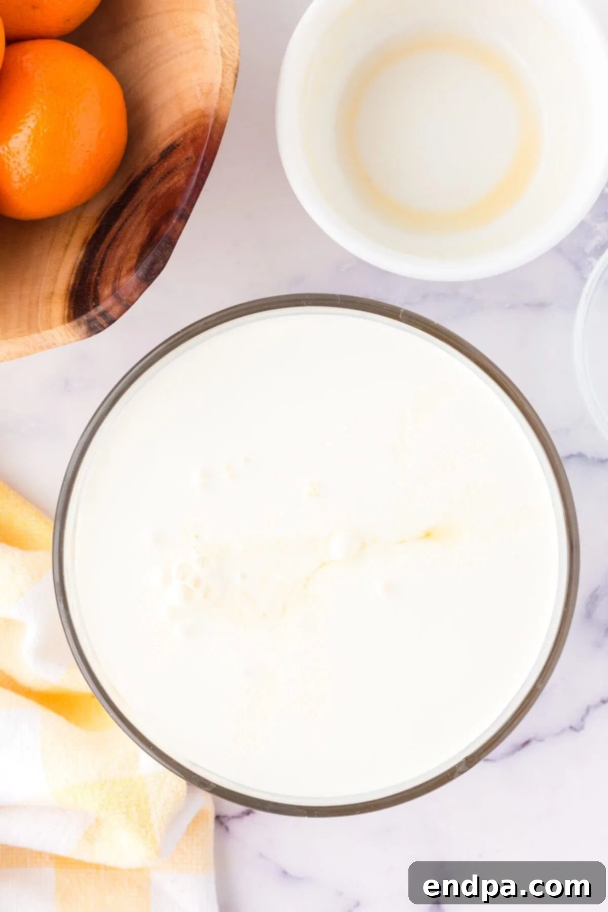 The creamy orange mixture for popsicles in a clear bowl before freezing.