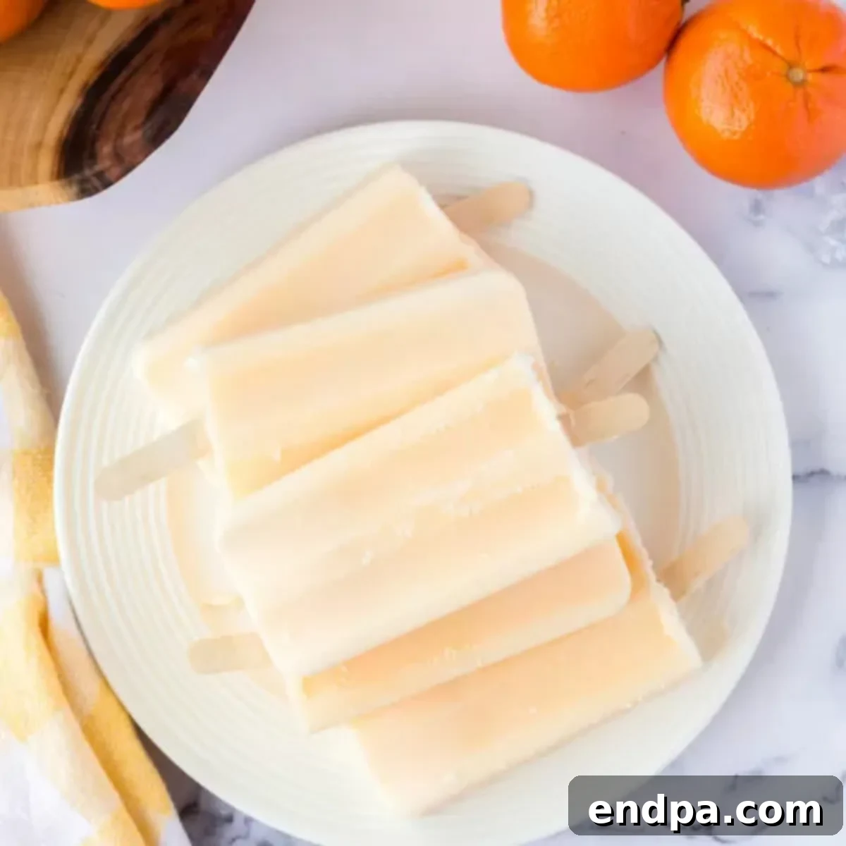 Orange popsicles on a white plate with fresh orange slices for garnish.