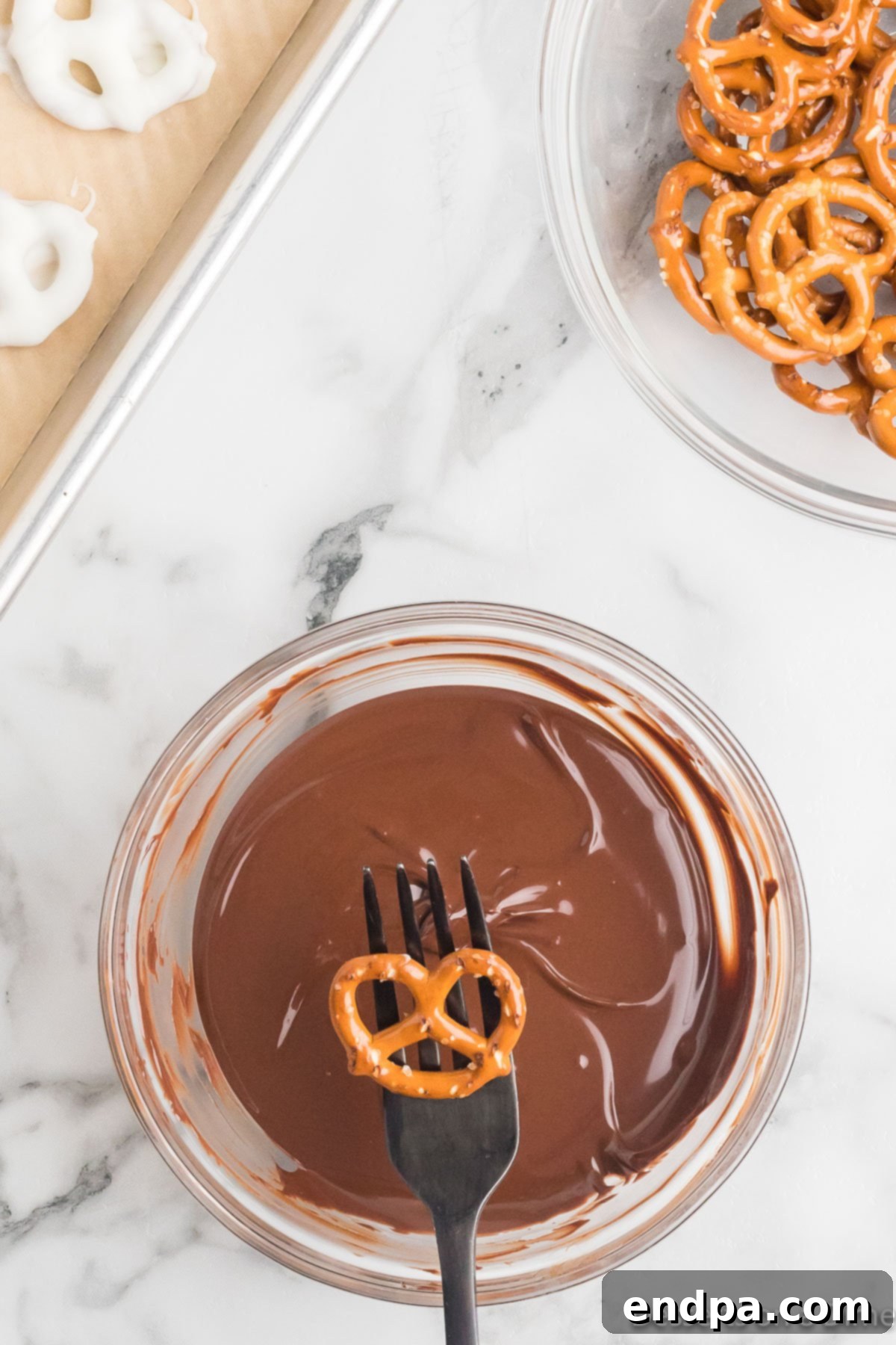 A pretzel poised on a fork, ready to be submerged into the rich milk chocolate.
