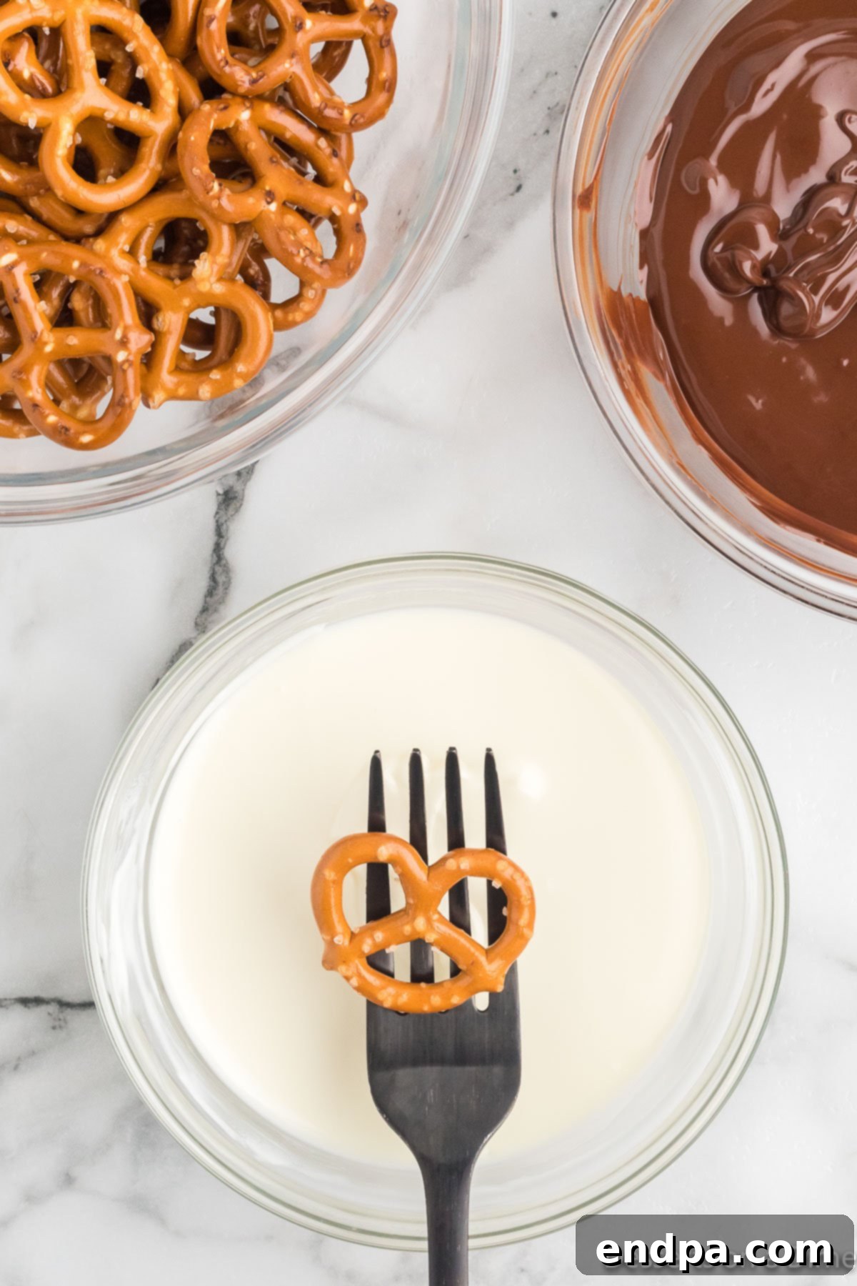 Another pretzel on a fork, about to enter the creamy white chocolate bath.