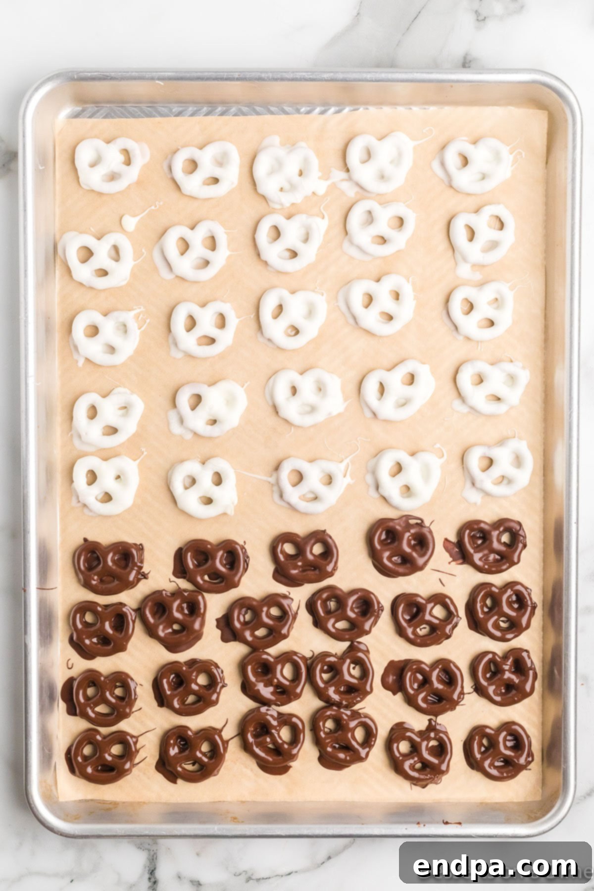 A baking sheet showcasing both white and milk chocolate covered pretzels, some already drizzled.