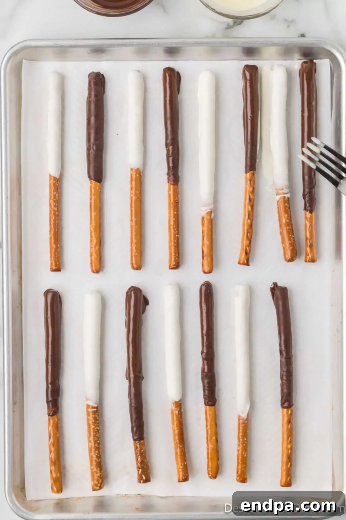 Pretzel Rods dipped in chocolate and drying on baking sheet.