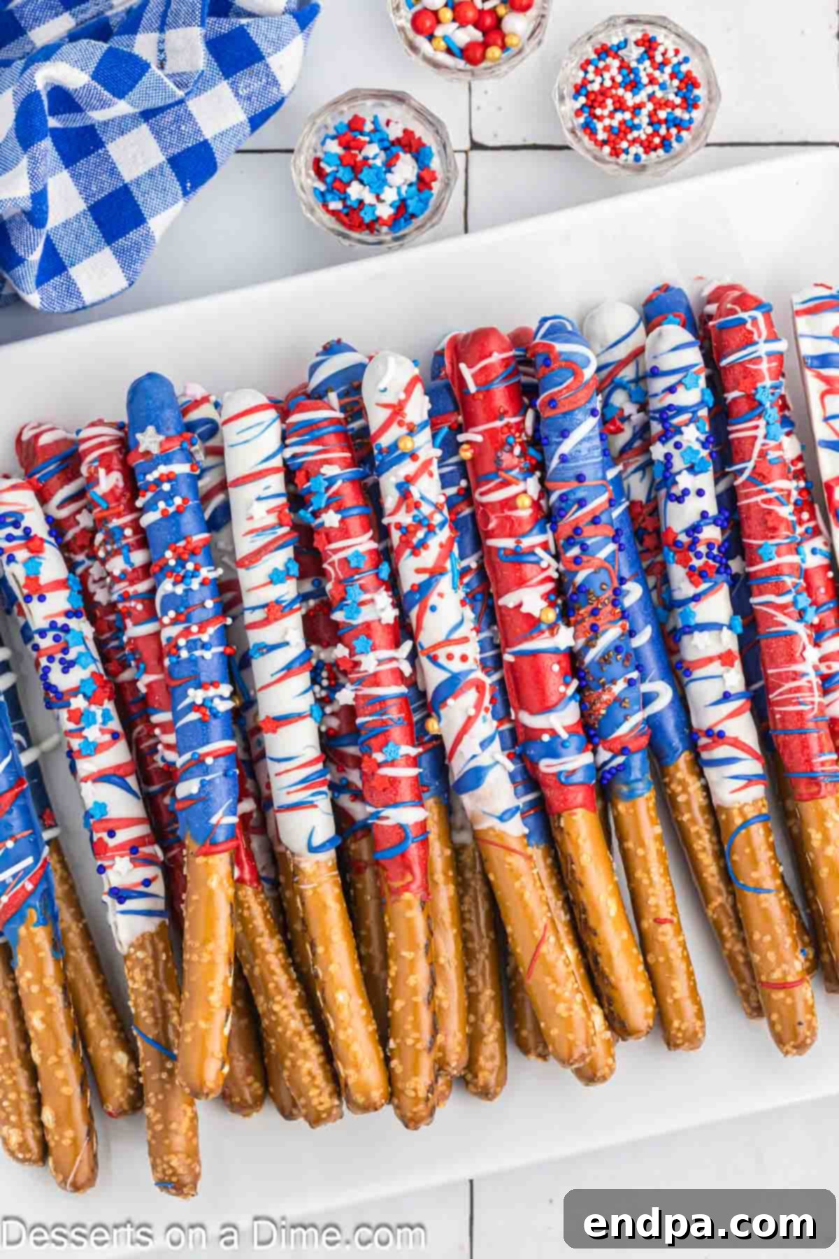 A collection of decorated 4th of July chocolate covered pretzel rods in a glass jar.