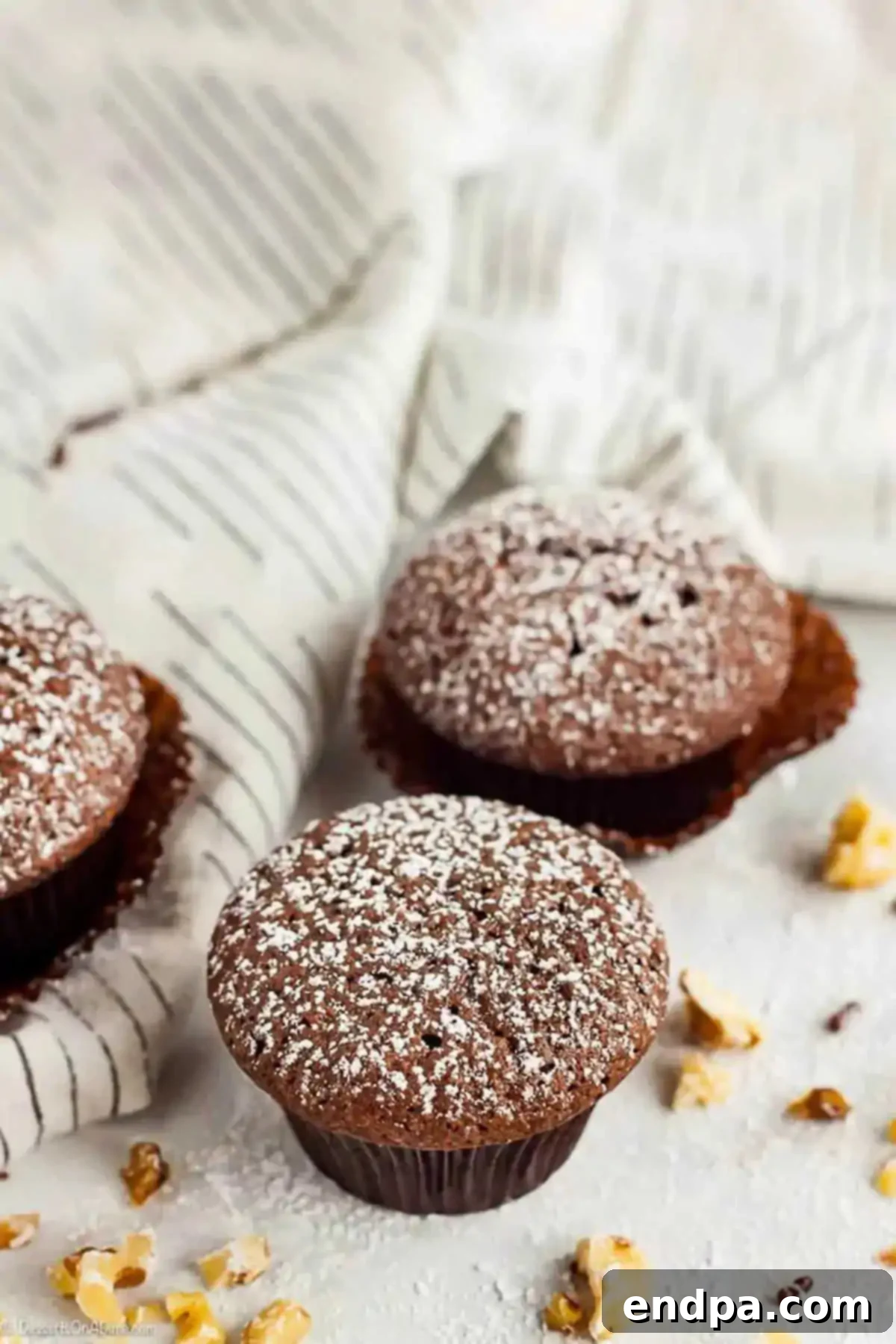 Indulge in these delightful Mini Brownie Cupcakes, perfect bite-sized treats bursting with rich chocolate flavor and incredibly easy to make. Each one is a decadent delight! Three Mini Brownie Cupcakes generously topped with powdered sugar, resting on a white surface with delicate chocolate drizzles and sprinkles scattered around.