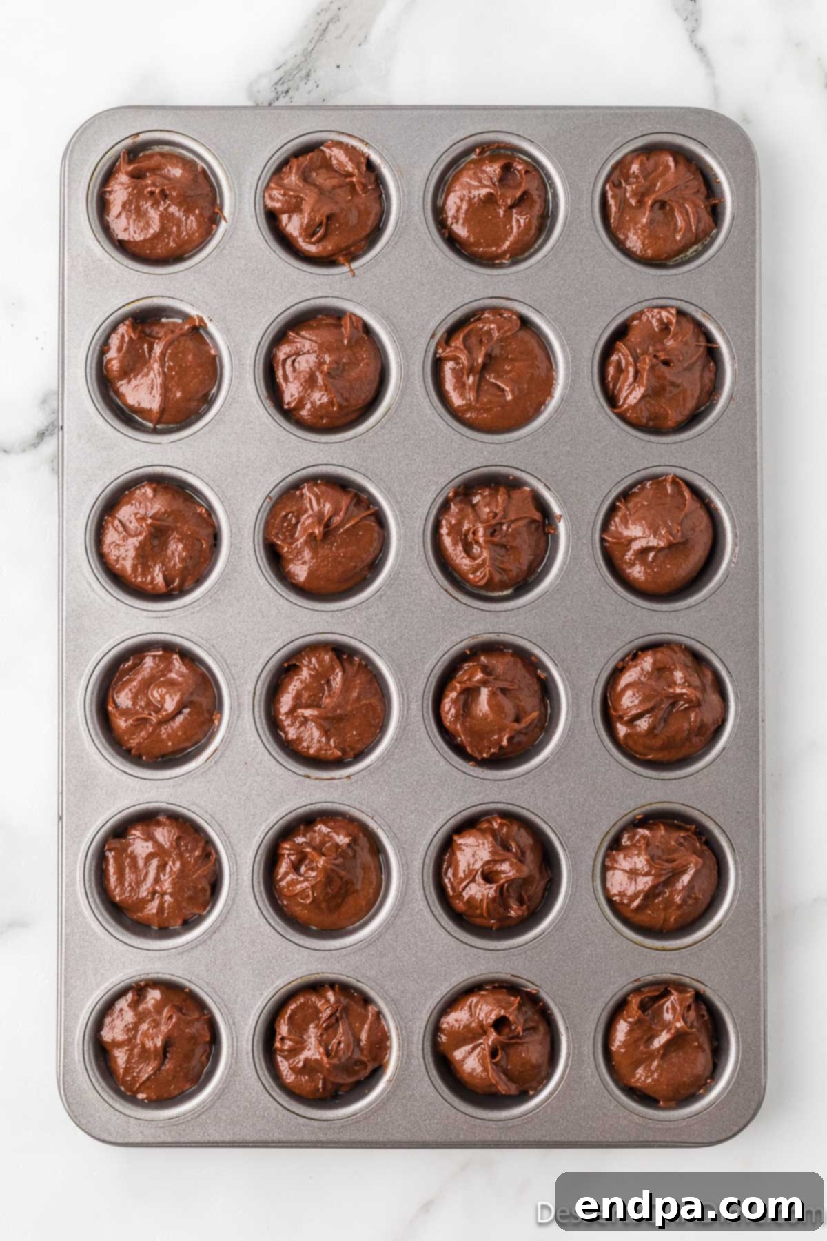 Bite-Sized Brownie Delights 4 Rich chocolate brownie batter being carefully spooned into a mini muffin pan, filling each cup evenly and ready for baking.